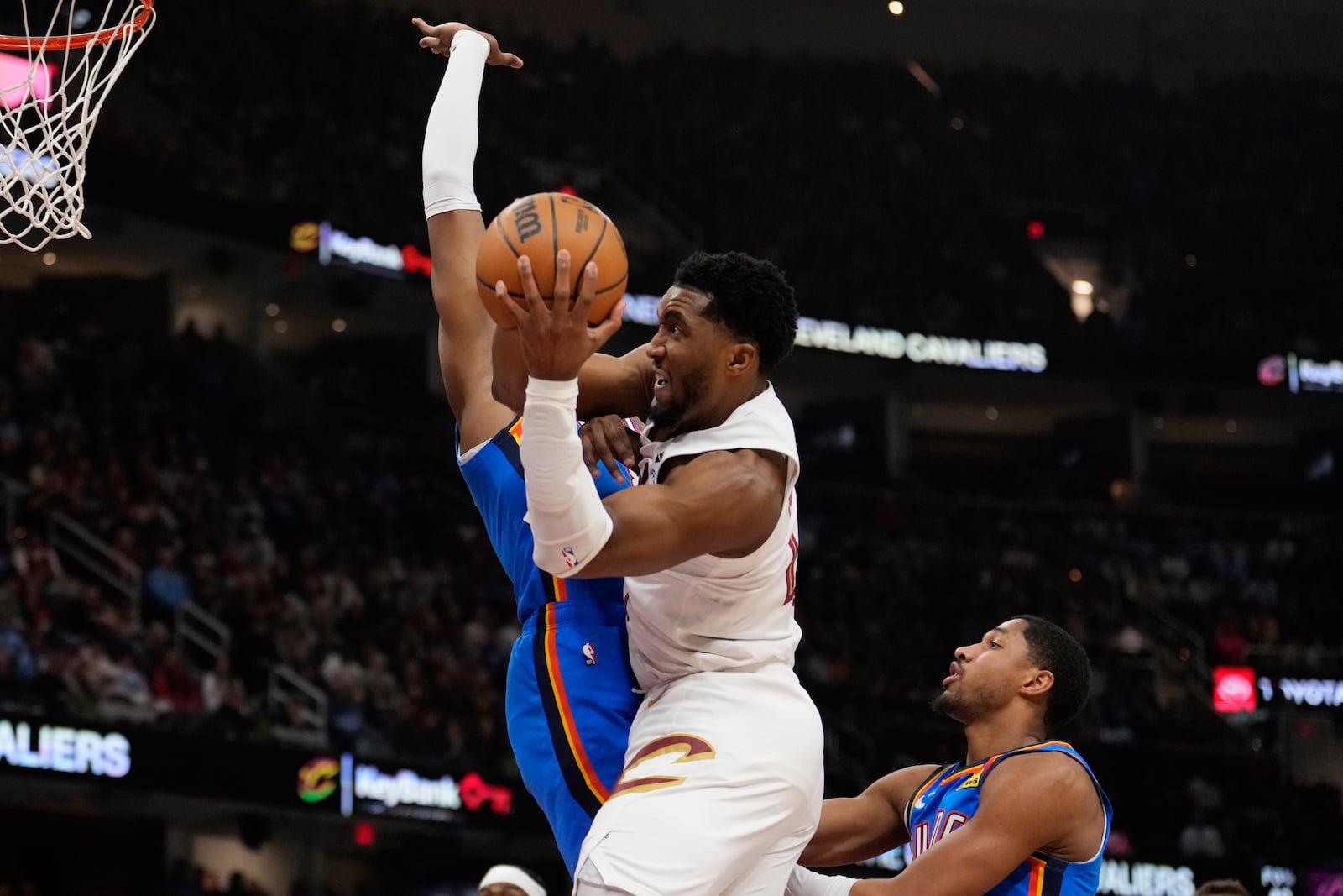 Cleveland Cavaliers guard Donovan Mitchell, center, goes to the basket between Oklahoma City Thunder forward Jalen Williams, left, and guard Aaron Wiggins,in the first half of an NBA basketball game, Wednesday, Jan. 8, 2025, in Cleveland. (AP Photo/Sue Ogrocki)