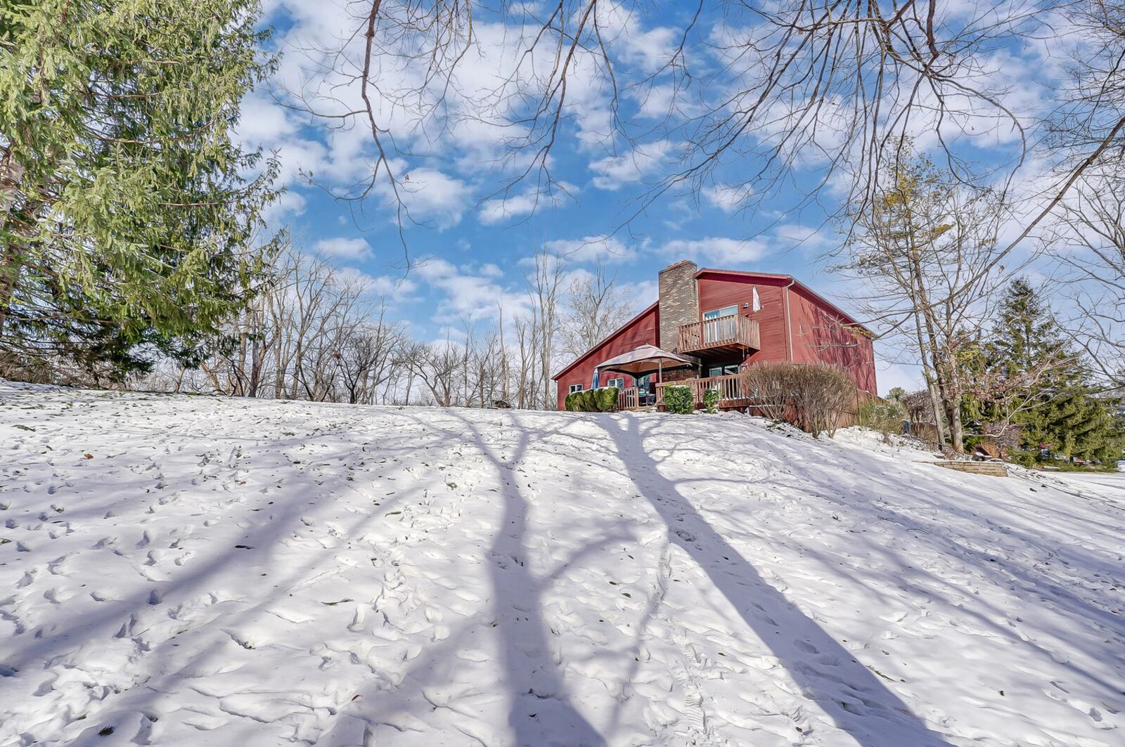 The rear of the home has a wood deck with railings and a wood deck/balcony on the upper level. The lot is tree-lined.