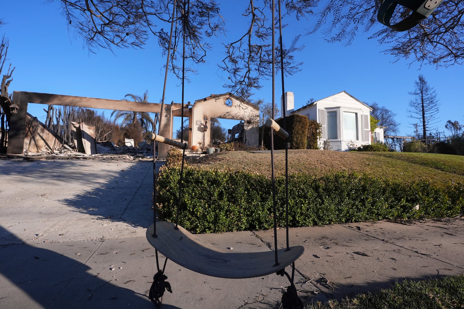 A swing hangs in front of an intact home and a home destroyed by the Palisades Fire in the Pacific Palisades neighborhood of Los Angeles, Sunday, Jan. 12, 2025. (AP Photo/Mark J. Terrill)