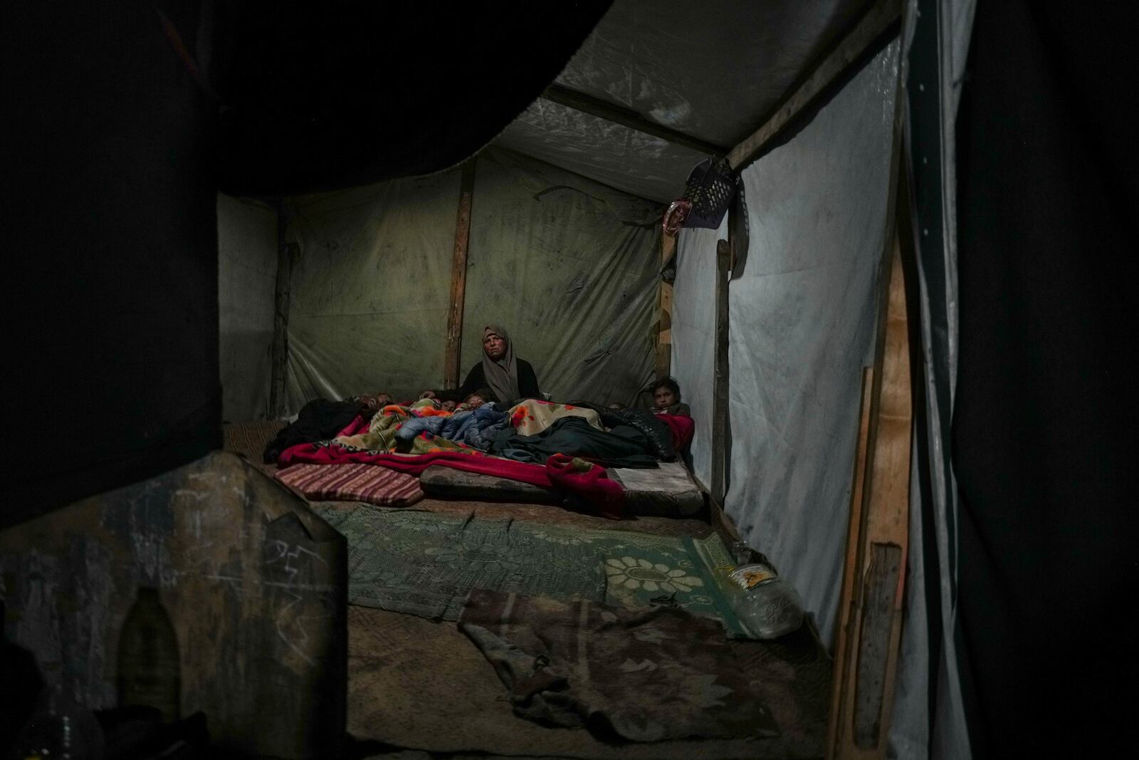 Reda Abu Zarada wraps herself and her grandchildren in blankets as they prepare to sleep in their tent at a camp in Khan Younis, Gaza Strip, Thursday, Dec. 19, 2024. (AP Photo/Abdel Kareem Hana)