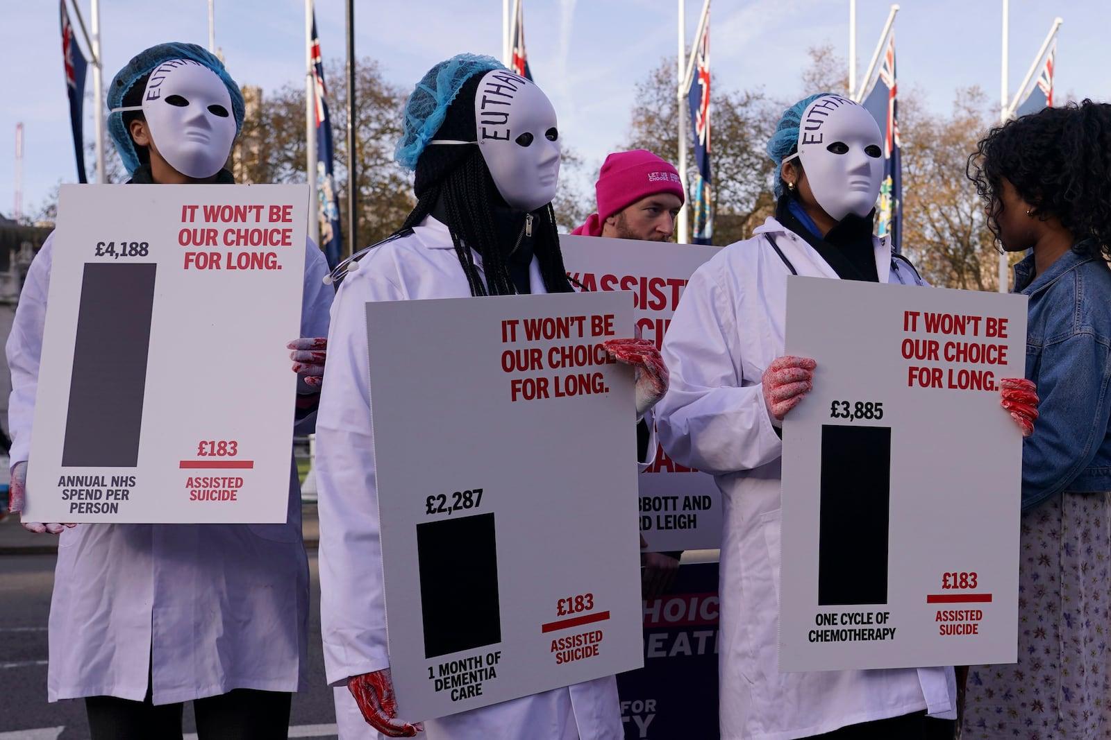 Protesters wearing masks show placards in front of Parliament in London, Friday, Nov. 29, 2024 as British lawmakers started a historic debate on a proposed to help terminally ill adults end their lives in England and Wales.(AP Photo/Alberto Pezzali)