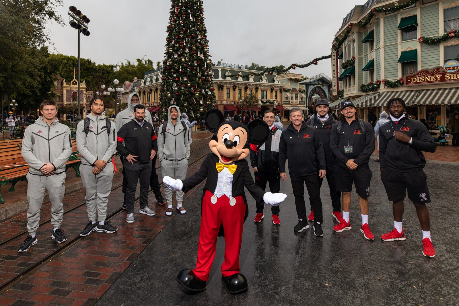 The head football coaches and select players from The Ohio State University Buckeyes and the Utah Utes pose for a photo with Mickey Mouse at Disneyland Park, in Anaheim, Calif., Dec. 27, 2021. From left to right: Bryson Shaw, C.J. Stroud, Ryan Day, Dawand Jones, Jaxon Smith-Njigba, Britain Covey, Kyle Whittingham, Mika Tafua, Cameron Rising and Devin Lloyd. The teams made their first stop on the way to the 2022 Rose Bowl Game presented by Capital One Venture X in Pasadena, Calif., with a traditional visit to the Disneyland Resort. (Christian Thompson/Disneyland Resort)