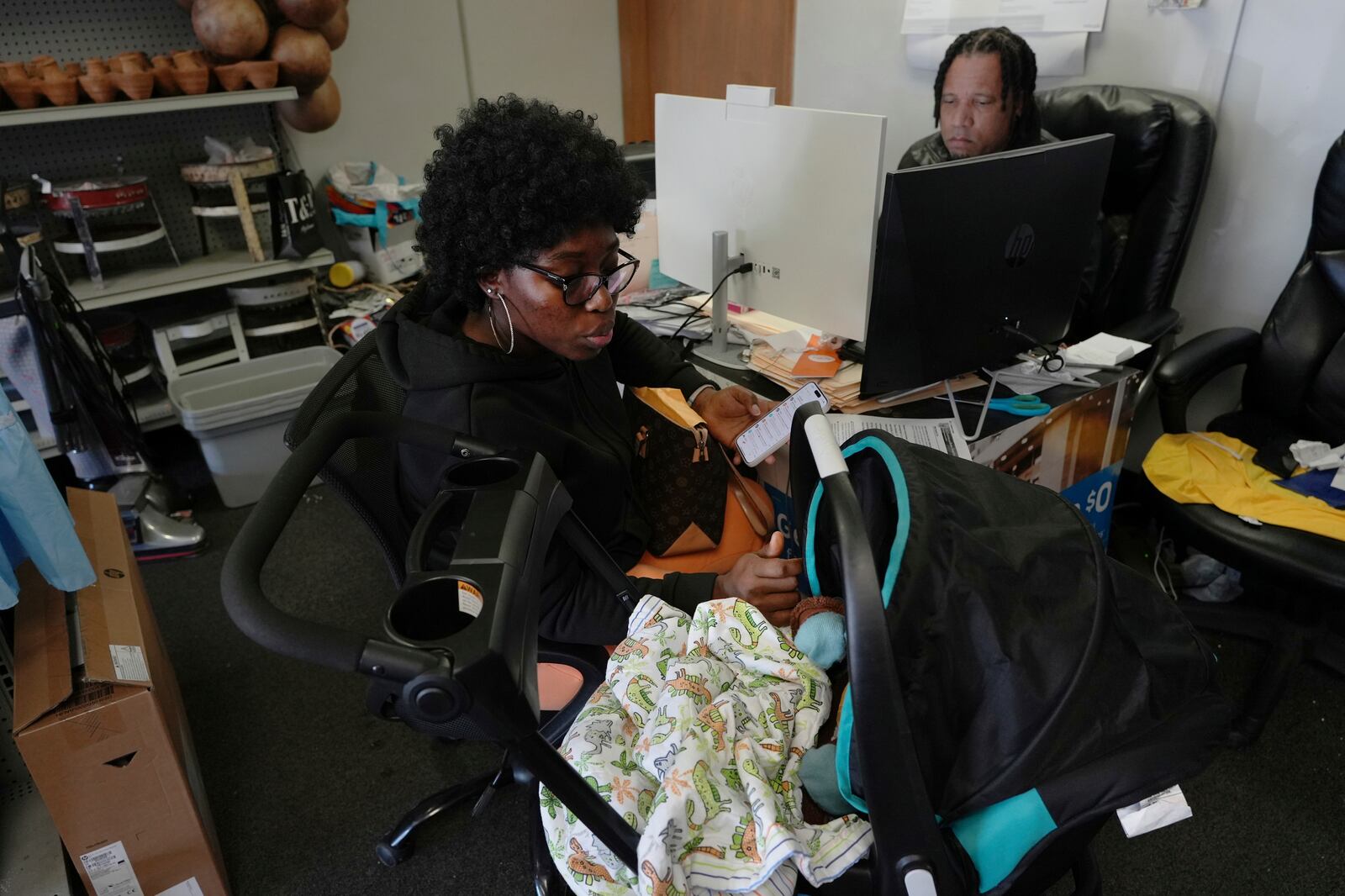 Dieutela Charles comforts her 6-month-old daughter while getting guidance on her U.S. residency from Haitian community leader Jacob Payton at his store in Springfield, Ohio, on Saturday, January 25, 2025. (AP Photo/Luis Andres Henao)