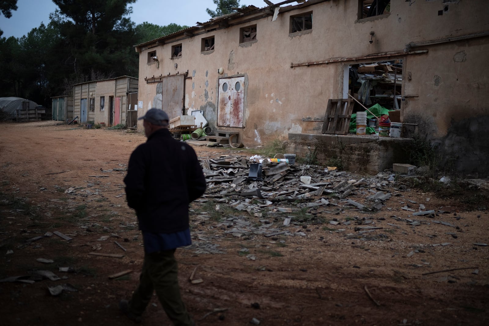 Dean Sweetland walks past a damaged warehouse that, according to him, was hit by a rocket fired from Lebanon two days before the start of the ceasefire between Israel and Hezbollah, in the Kibbutz Malkiya, northern Israel, Wednesday, Nov. 27, 2024. (AP Photo/Leo Correa)