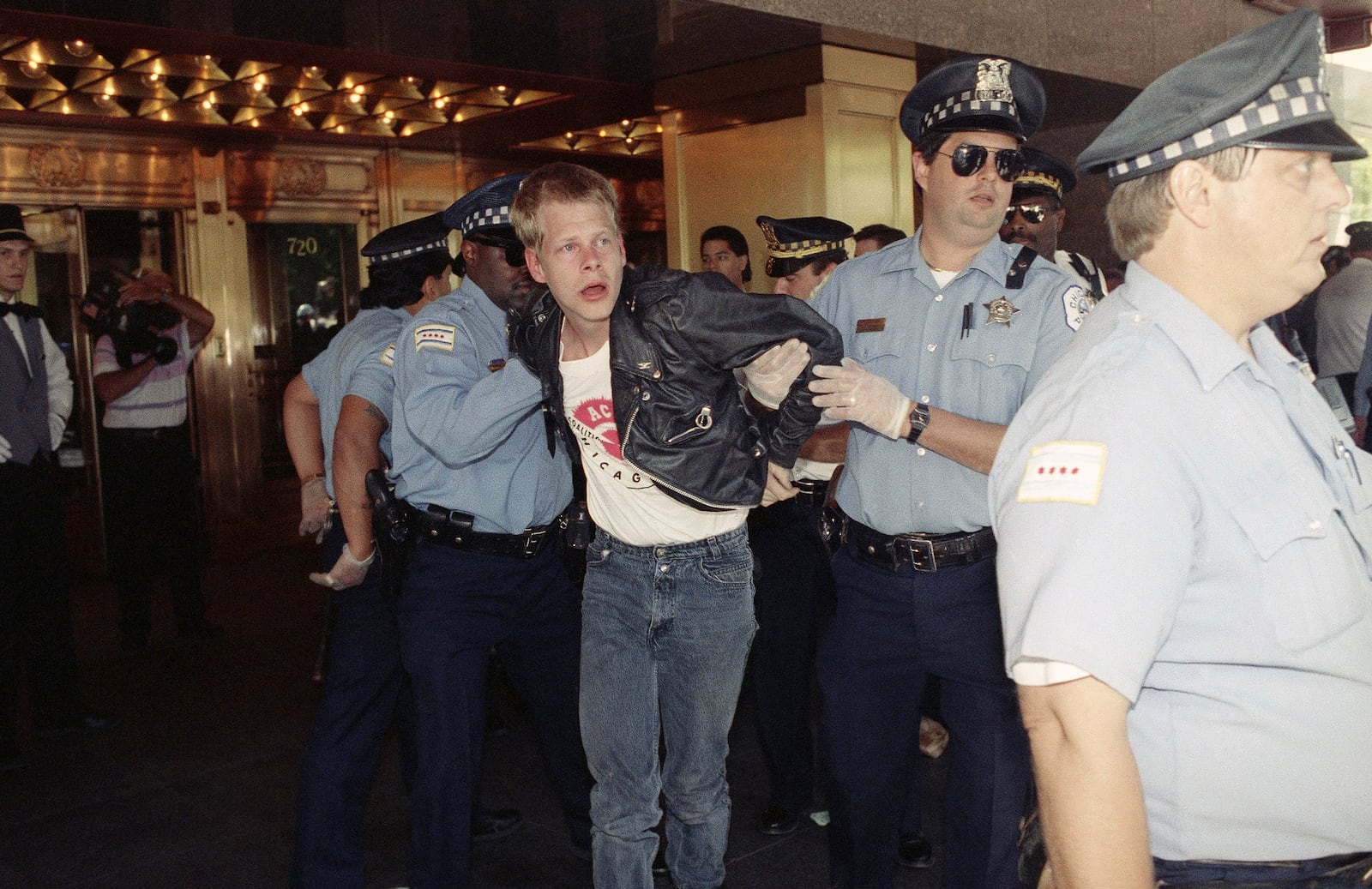 FILE - Chicago police officers, wearing rubber gloves, arrest a demonstrator outside the downtown hotel where the American Medical Association is holding its annual meeting in Chicago, June 24, 1991, as members of the AIDS Coalition to Unleash Power (ACT-UP) are protesting the AMA's AIDS policies. (AP Photo/John Swart, File)