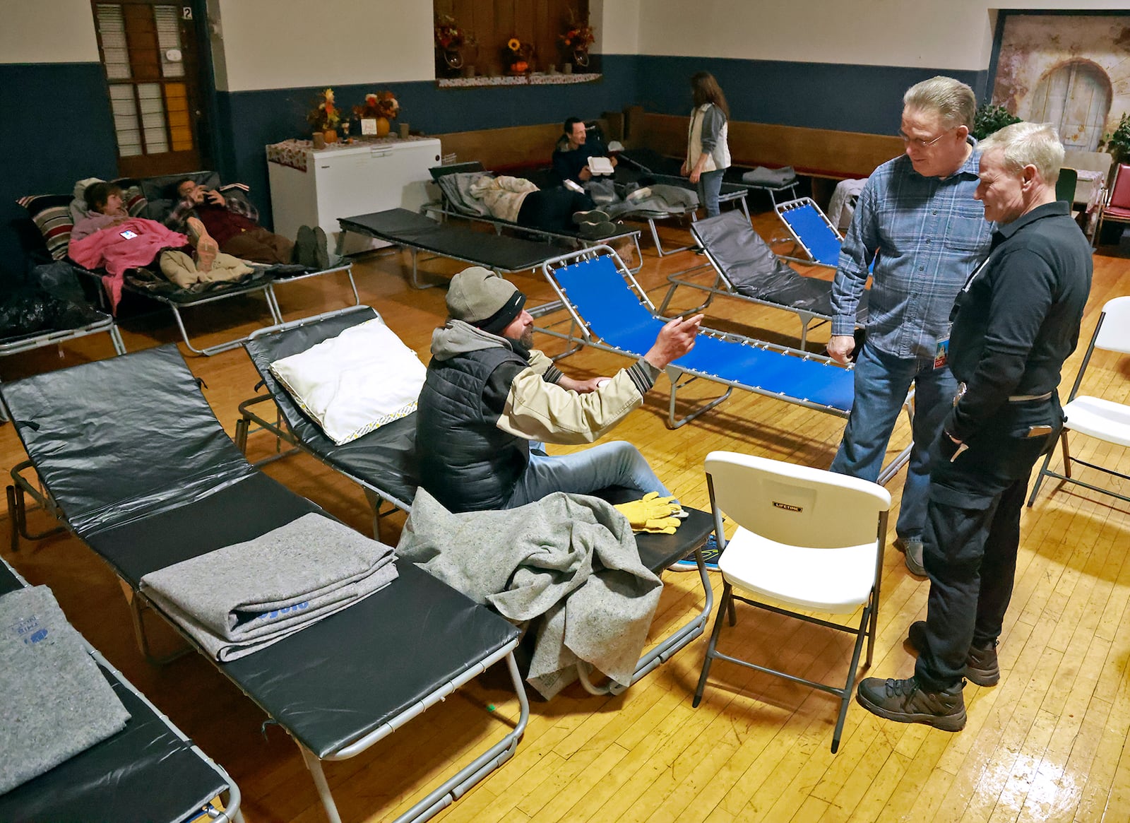 Volunteers talk with a man at the warming shelter in the Victory Faith Center gymnasium in early December 2024. The shelter was organized by Kenneth "Barron" Seelig with help from community volunteers as temperatures dropped below freezing outside. The shelter, which also offers a hot meal, opened for the first time on Monday. BILL LACKEY/STAFF