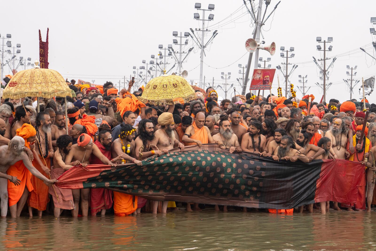 Hindu ascetics and holy men and their guru offer a cloth to the water as the prepare to bathe at the confluence of the Ganges, the Yamuna and the mythical Saraswati rivers on the second day of the 45-day-long Maha Kumbh festival in Prayagraj, India, Tuesday, Jan. 14, 2025. (AP Photo/Ashwini Bhatia)