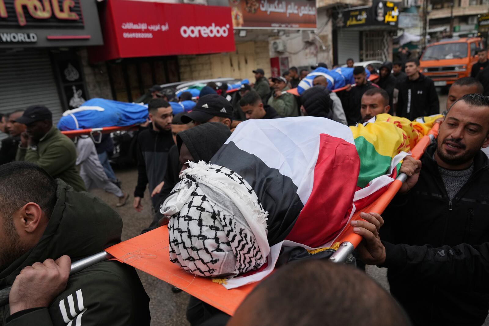 Mourners carry the bodies of four Palestinians killed after there vehicle was targeted by an Israeli airstrike in the refugee camp of Tulkarem on Thursday, one is wrapped with a Hamas flag, during their funeral in the West Bank city of Tulkarem Friday, Dec.20, 2024. (AP Photo/Nasser Nasser)