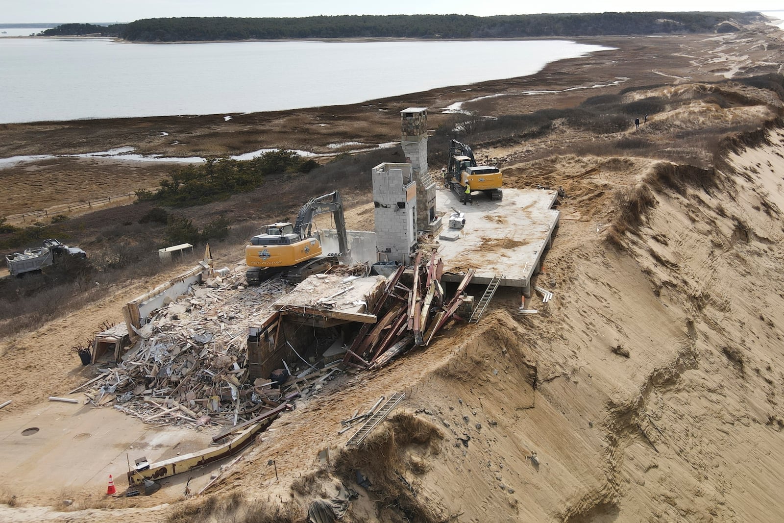 The remains of a home sit atop of a sandy bluff overlooking a beach in Wellfleet, Mass., Tuesday, Feb. 25, 2025. (AP Photo/Andre Muggiati)