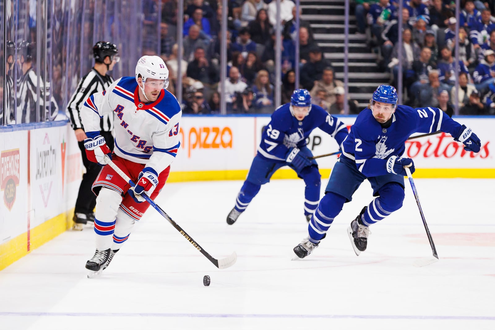 New York Rangers left wing Alexis Lafreniere (13) skates the puck up ice as he's trailed by Toronto Maple Leafs defenceman Simon Benoit (2) during first period NHL hockey action in Toronto on Saturday, October 19, 2024. (Cole Burston/The Canadian Press via AP)