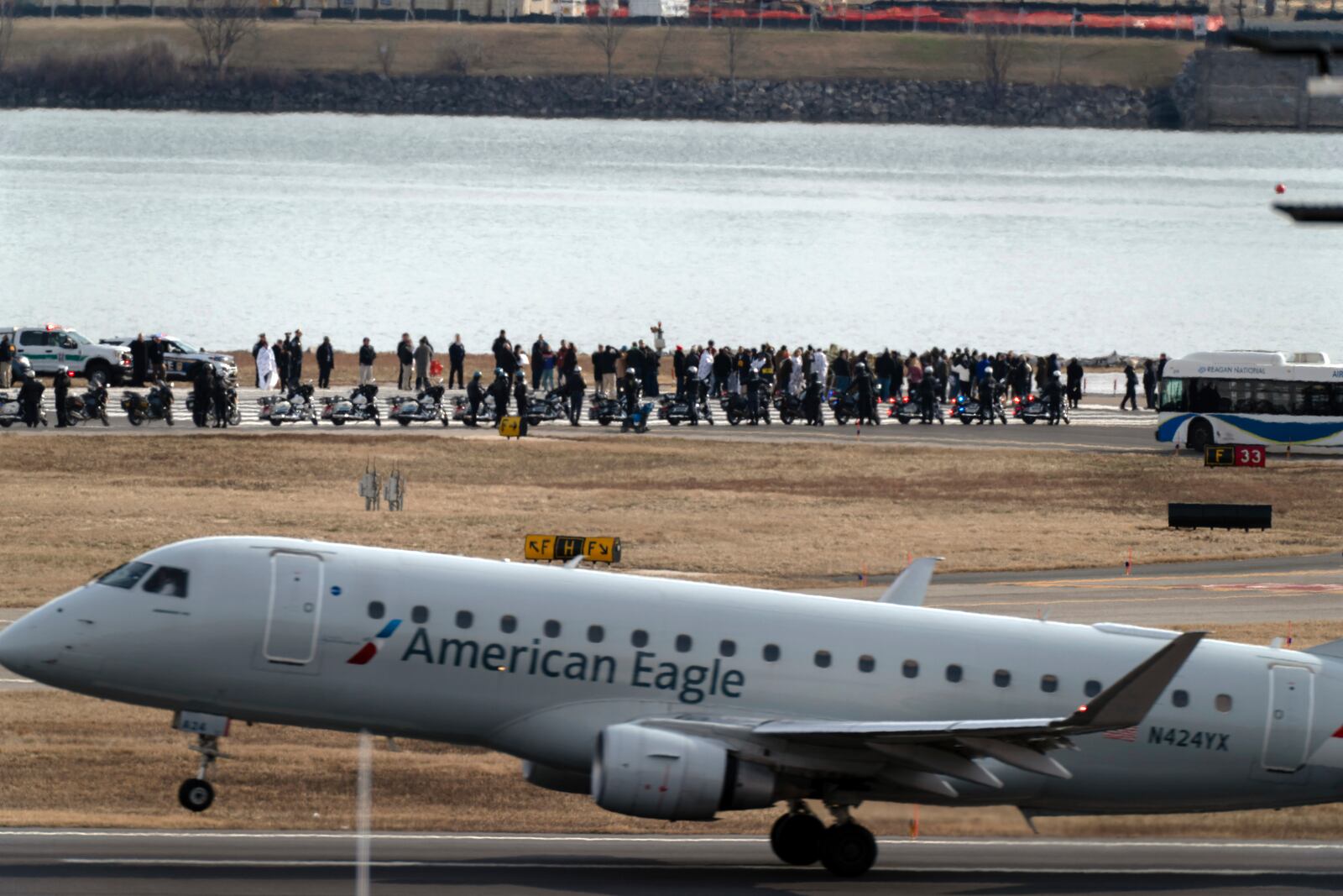 An American Eagle jet passes as families of the victims of a mid-air collision between an American Airlines jet and an Army helicopter stand near the wreckage site in the Potomac River at the end of the runway 33 from Ronald Reagan Washington National Airport, Sunday, Feb. 2, 2025, in Arlington, Va. (AP Photo/Jose Luis Magana)