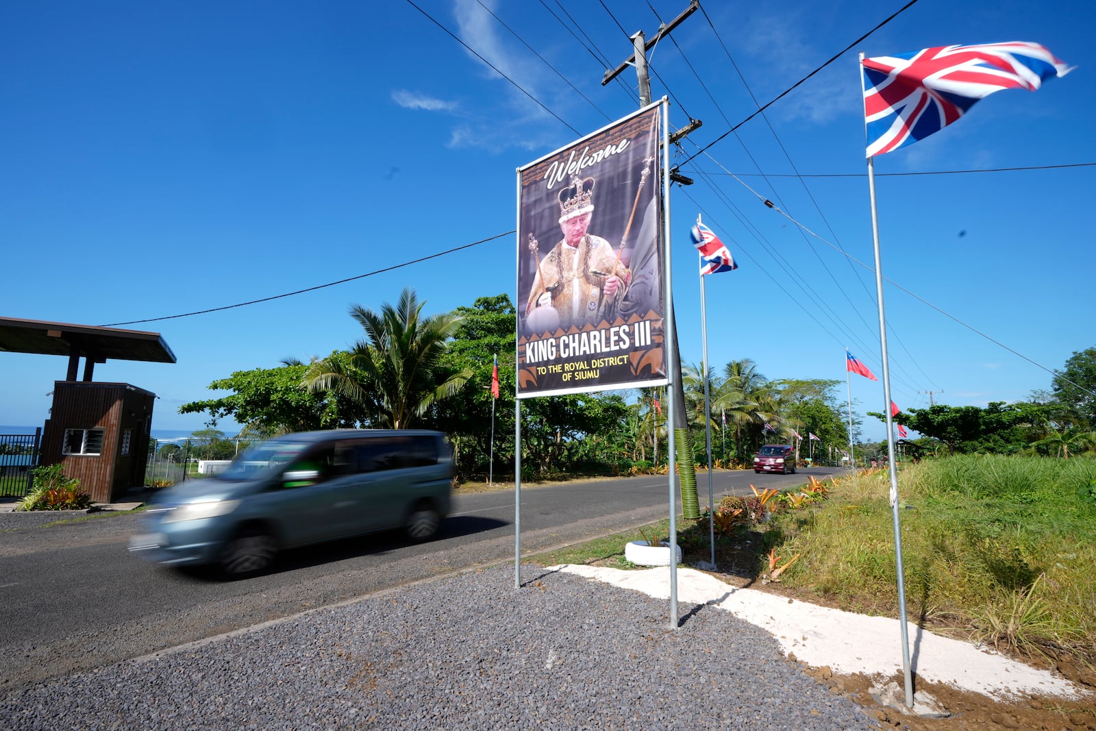 A car drives on a road decorated with flags and a portrait in the village of Siumu, Samoa, on Monday, Oct. 21, 2024, as the village prepares for the arrival of King Charles III. (AP Photo/Rick Rycroft)