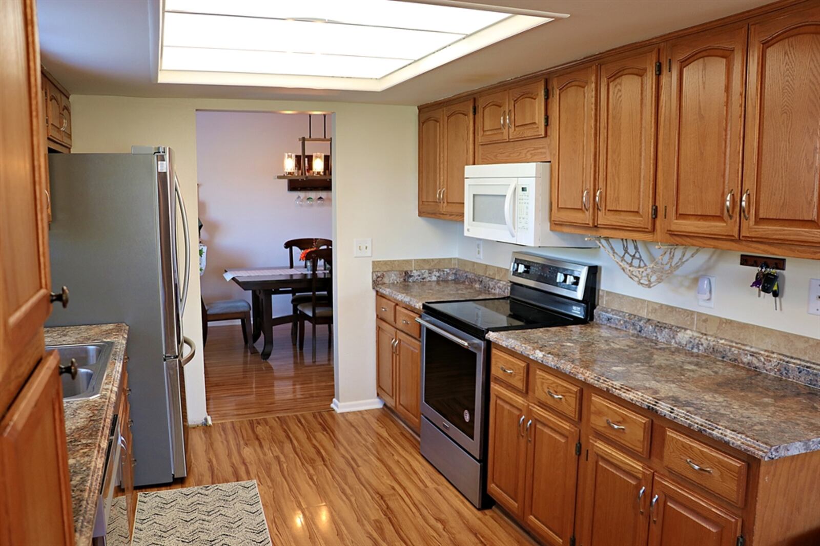 The galley kitchen has an abundance of oak cabinetry with complementary counters. There is a pantry cabinet, and a window is above the double stainless-steel sink. Recessed lighting fills the kitchen with plenty of light.