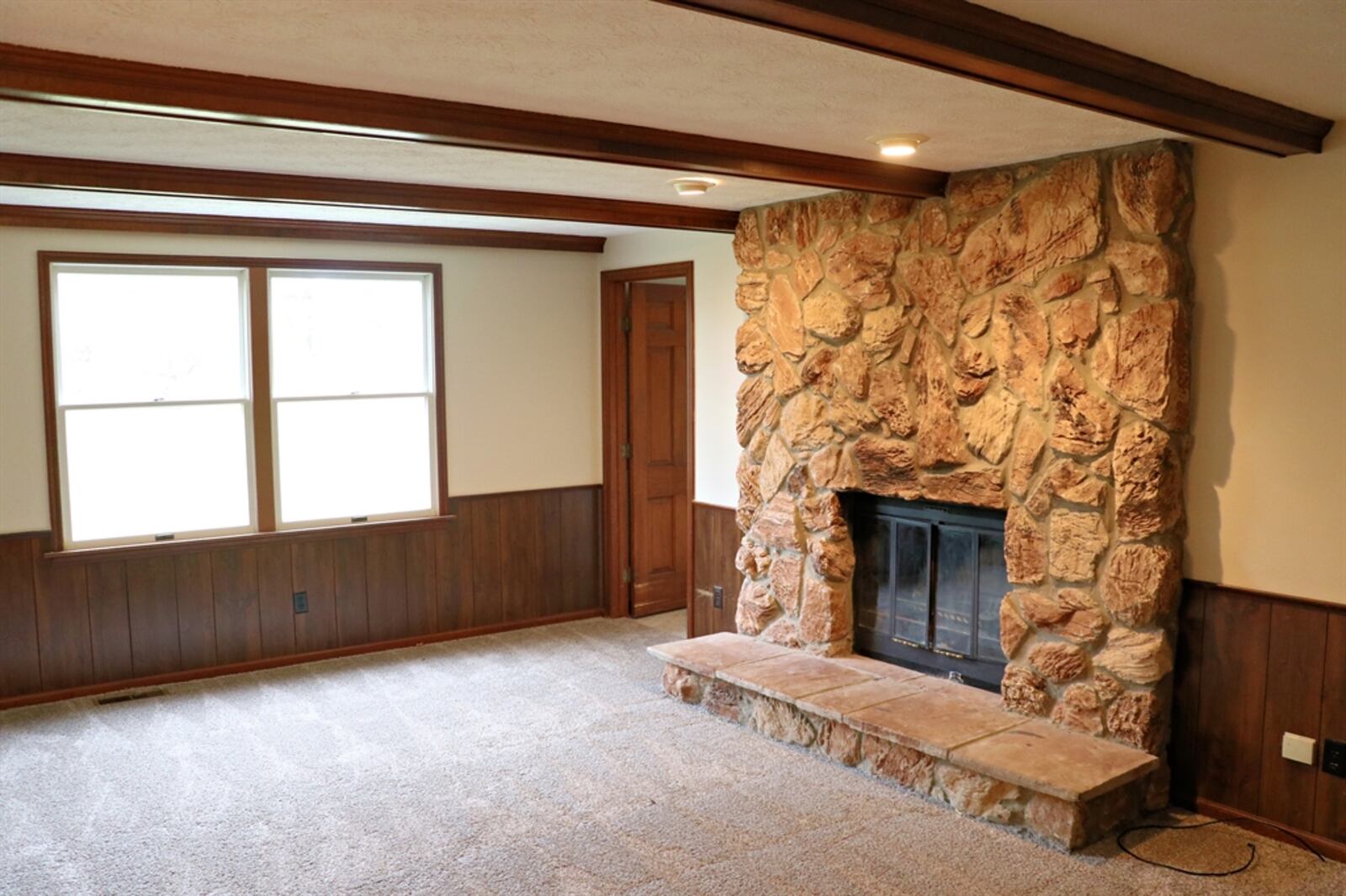 The spacious family room has a stone fireplace with a raised stone hearth. Wood beams accent the ceiling and complement the partial paneled walls. Between the family room and the foyer, a set of bi-fold closet doors open into a surprise wet bar nook.
