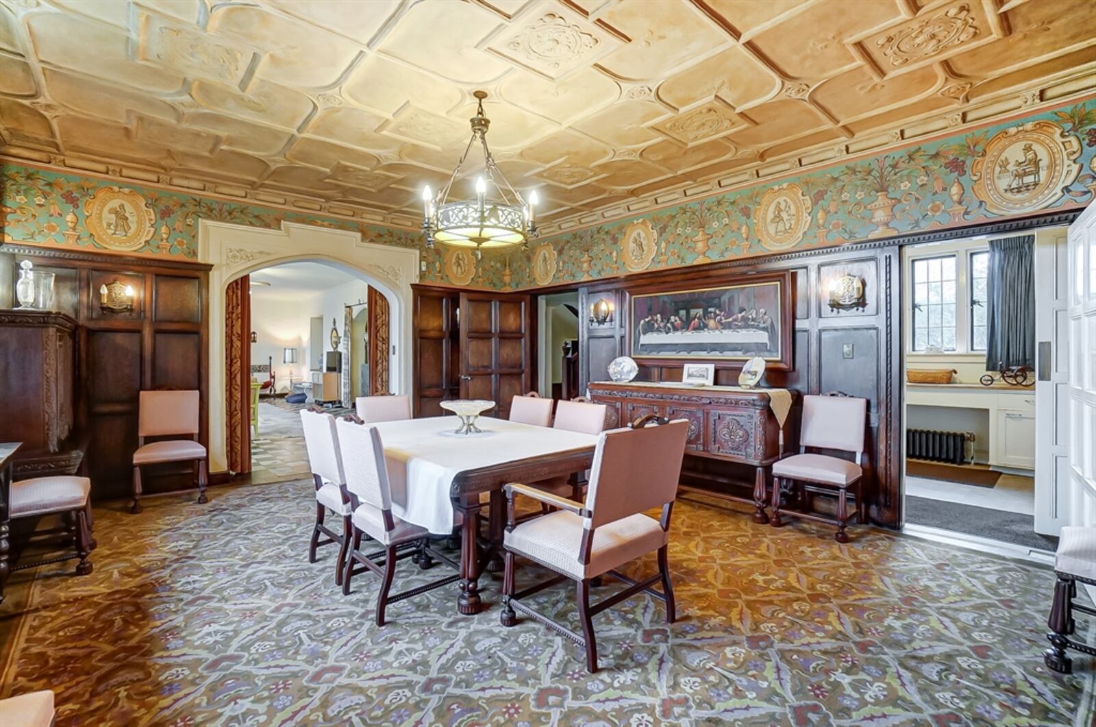 Curtain-covered threshold leads into the formal dining room, which has walnut judge’s paneling and artwork rail. The stucco coffered ceiling has many fleur-de-lis reliefs. 