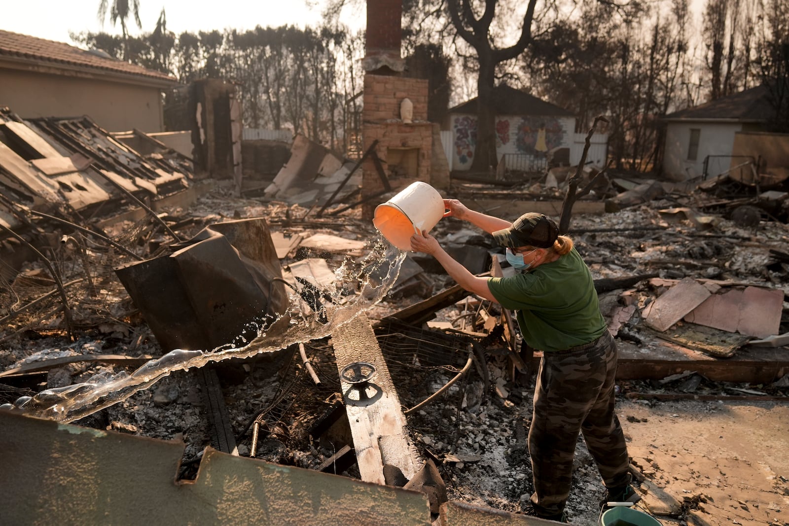 FILE - Nancy Belanger pours water on a neighbor's fire-ravaged property in the aftermath of the Palisades Fire in the Pacific Palisades neighborhood of Los Angeles, Thursday, Jan. 9, 2025. (AP Photo/Jae C. Hong,File)