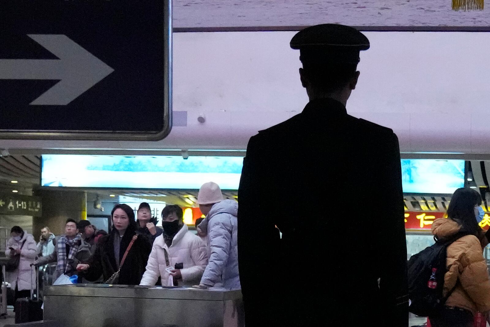 A security person watches travelers at the Beijing West Railway Station as families travel back home ahead of the Lunar New Year in Beijing on Friday, Jan. 24, 2025. (AP Photo/Aaron Favila)