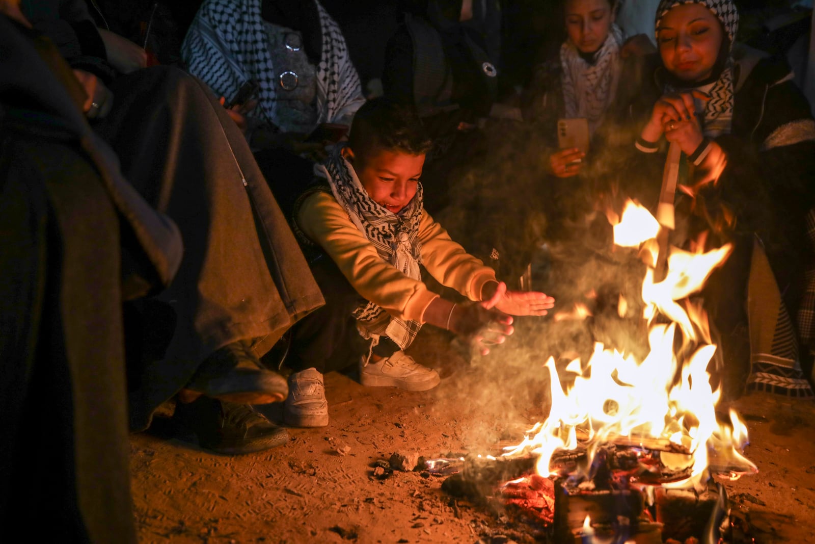 A boy warms up as families and friends of Palestinian prisoners to be released from Israeli prison wait around a bonfire for their arrival in Khan Younis, southern Gaza Strip, late Wednesday Feb. 27, 2025. (AP Photo/Jehad Alshrafi)