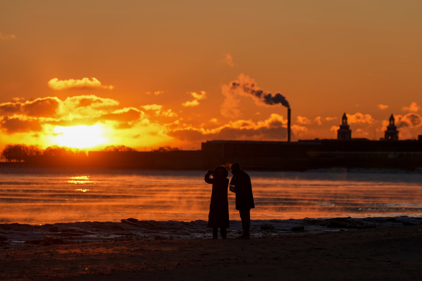 A couple take pictures at sunrise from the icy Oak Street Beach along the shore of Lake Michigan Monday, Jan. 20, 2025, in Chicago, as the weather service issued cold weather advisories across the Great Lakes region as high temperatures in many places were expected only to rise into the single digits Monday and Tuesday. (AP Photo/Kiichiro Sato)