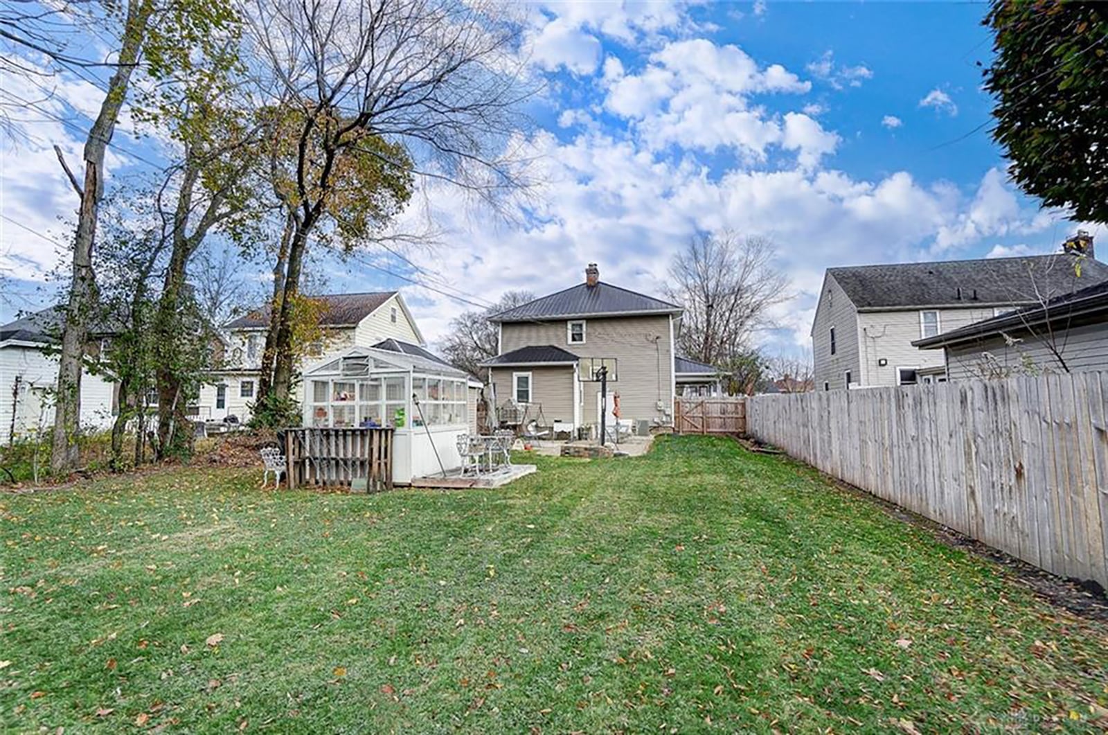 The rear of the home has a partial privacy fence, greenhouse with deck, paver patio and detached one-car garage. 