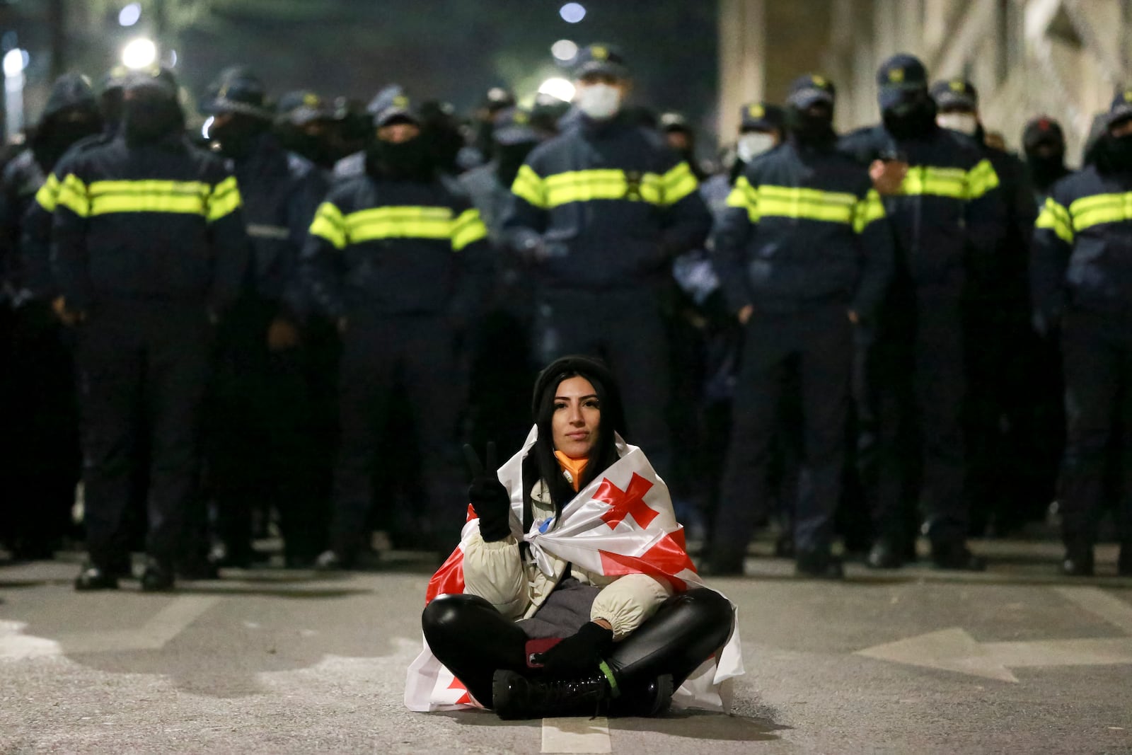 A demonstrator draped in a Georgian national flag sits in front of police rallying outside the parliament's building to continue protests against the government's decision to suspend negotiations on joining the European Union in Tbilisi, Georgia, on Monday, Dec. 2, 2024. (AP Photo/Zurab Tsertsvadze)