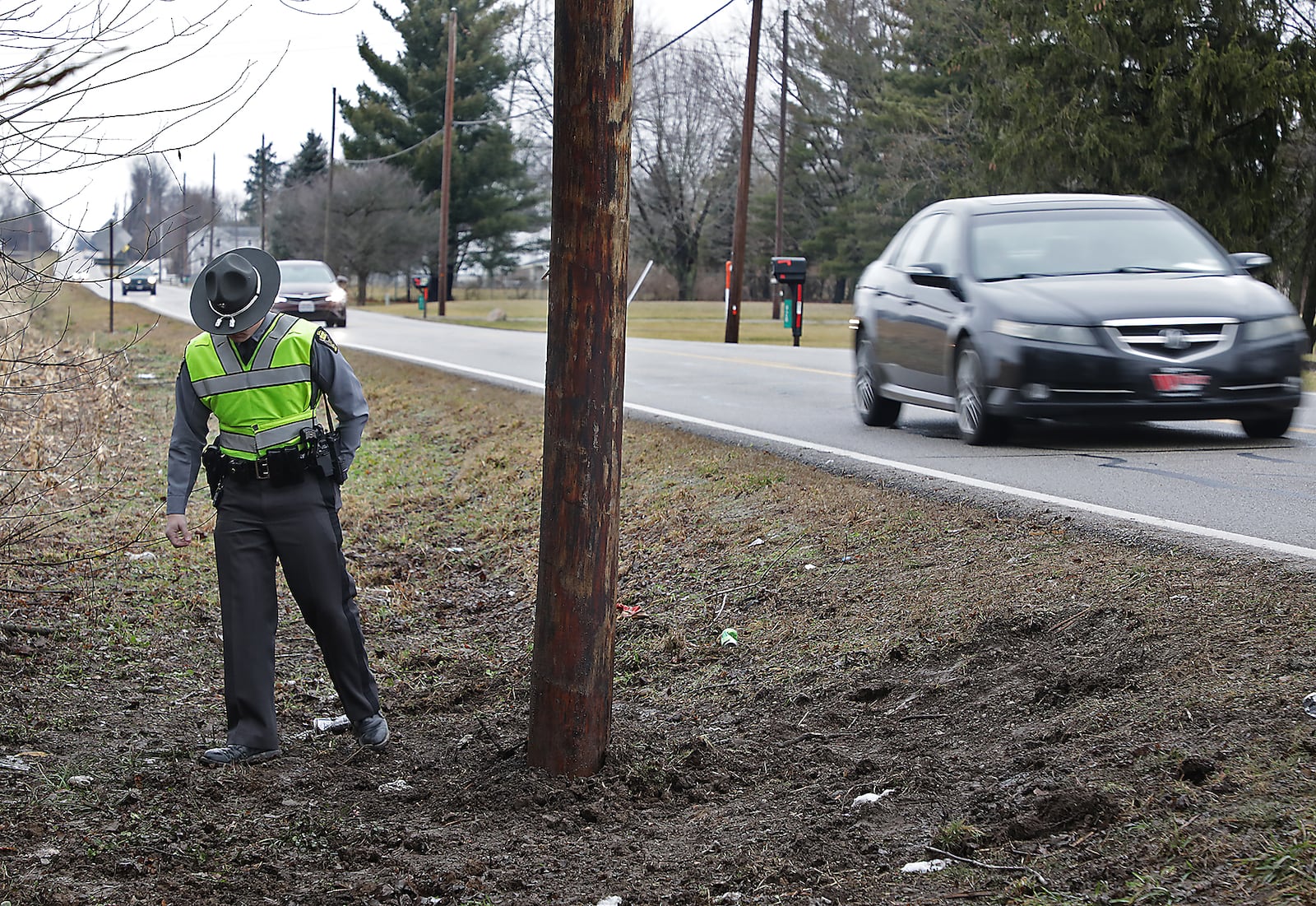 A member of the Ohio Highway Patrol helps family members look for a cell phone around the utility pole that Jason Whitt struck along Medway-New Carlisle Road Sunday night. Whitt, 17, was killed in the crash. Three other teenagers in the car were injured. BILL LACKEY/STAFF