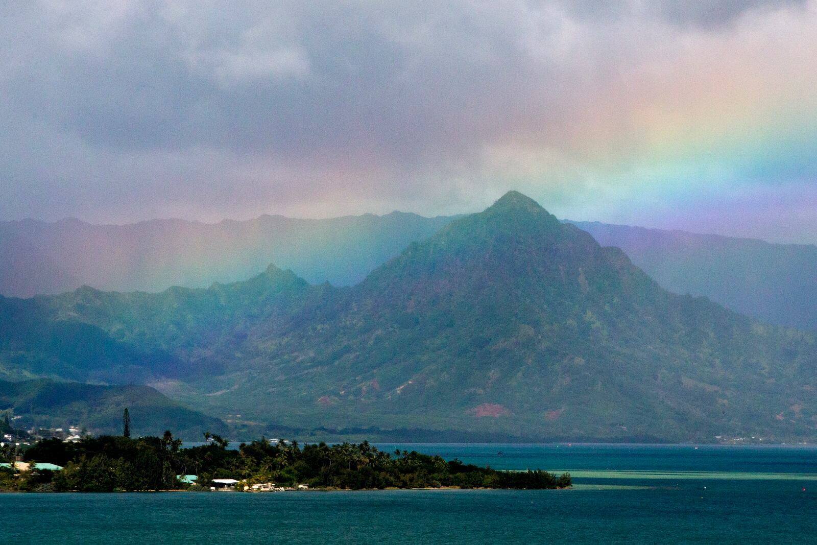 FILE -A rainbow is seen in the sky from President Barack Obama's motorcade as it passes Kaneohe Bay heading for the beach at Bellows Air Force Station, Saturday, Jan. 3, 2015, on the island of Oahu in Hawaii, on the final day of the Obama family vacation. (AP Photo/Jacquelyn Martin, File)