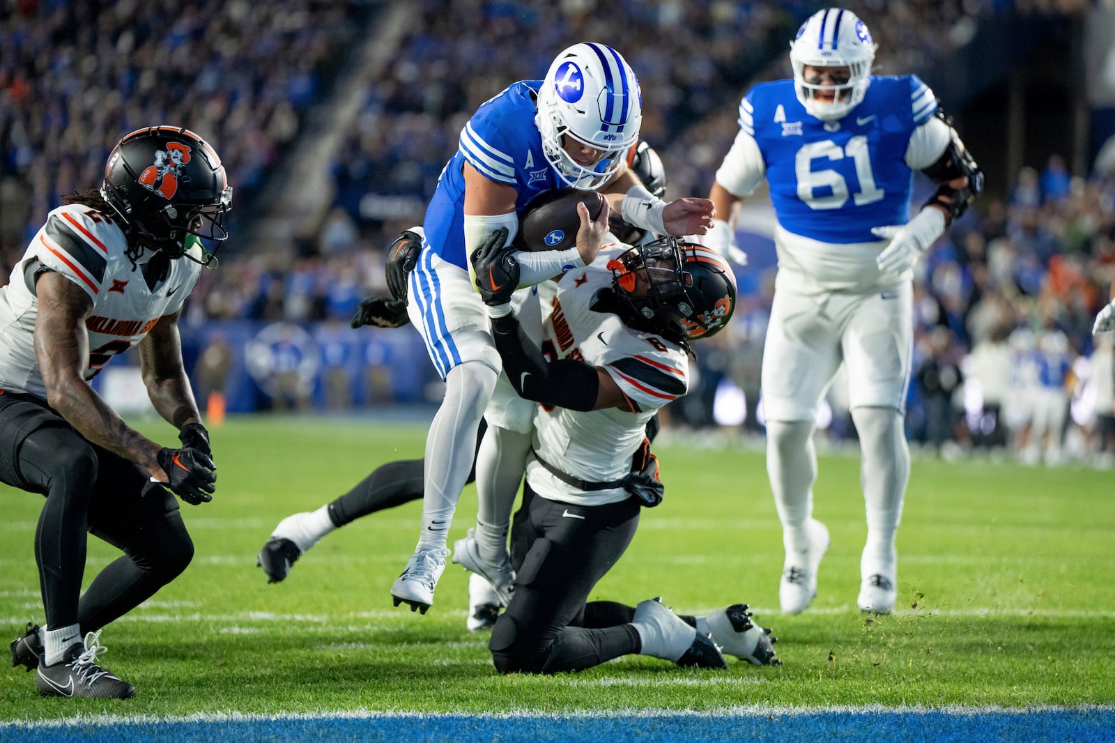 BYU quarterback Jake Retzlaff, center top, runs the ball for a touchdown past a tackle-attempt by Oklahoma State safety Lyrik Rawls, center bottom, in the first half of an NCAA college football game, Friday, Oct. 18, 2024, in Provo, Utah. (AP Photo/Spenser Heaps)