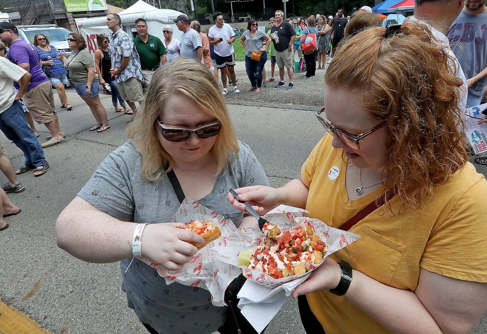 Natalie Cochran, left, and Sarah McGee-Gentry enjoy their lobster dishes that they waited in the long line for, in the background, Saturday during the Springfield Rotary Gourmet Food Truck Competition. BILL LACKEY/STAFF