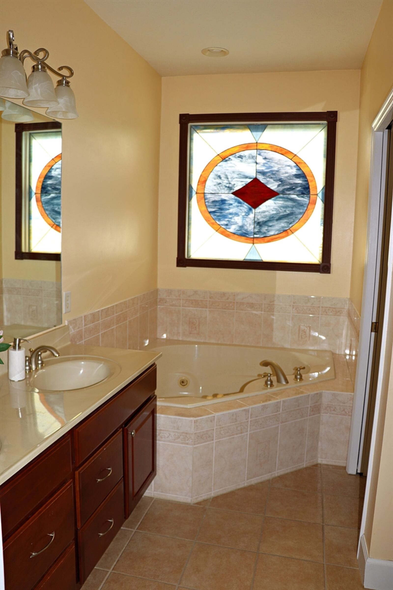 The primary bath has a double-sink vanity and a corner whirlpool tub below a stained-glass window. 