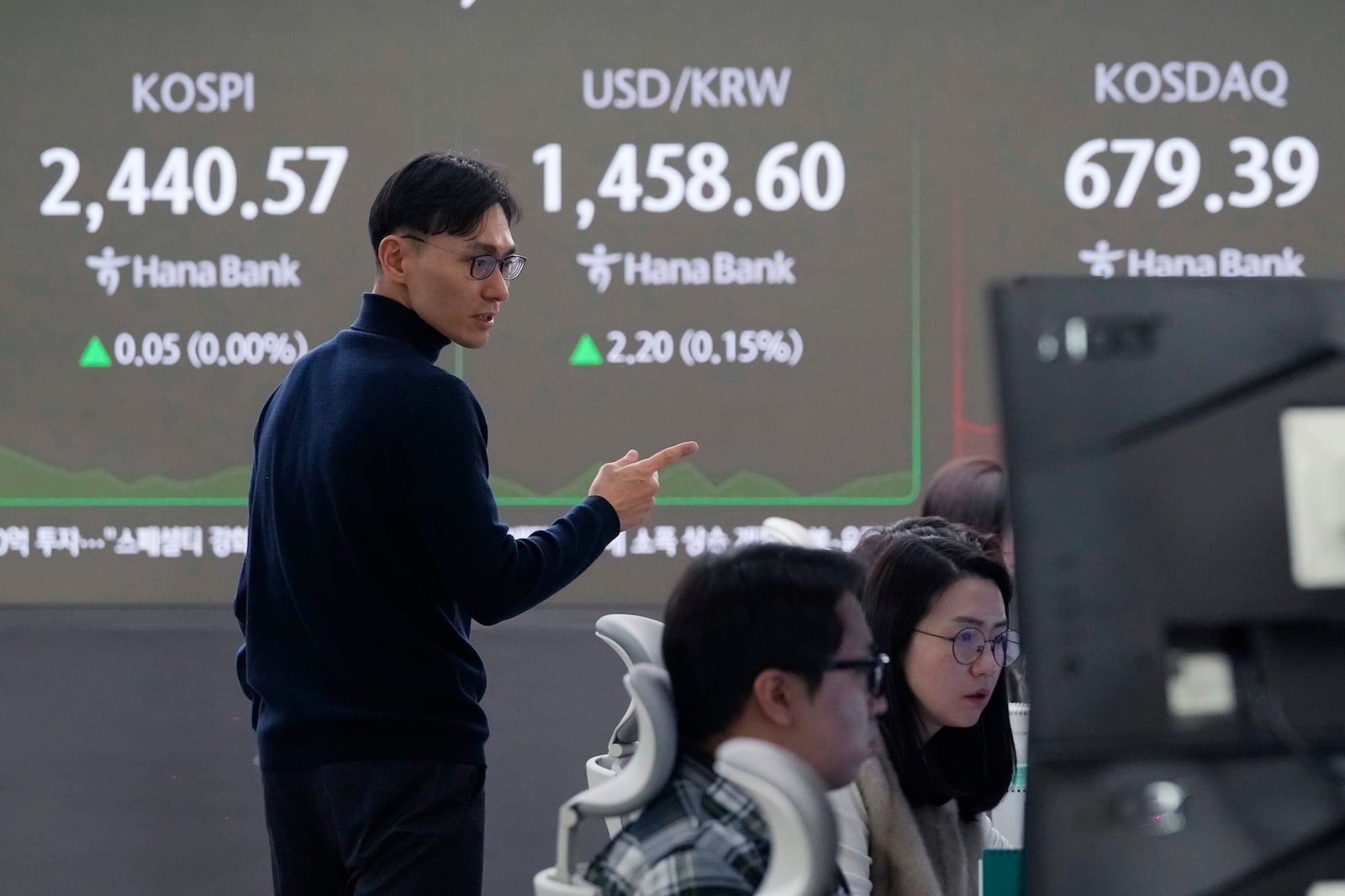 A currency trader talks to another near a screen showing the Korea Composite Stock Price Index (KOSPI), top left, and the foreign exchange rate between U.S. dollar and South Korean won, top center, at the foreign exchange dealing room of the KEB Hana Bank headquarters in Seoul, South Korea, Thursday, Dec. 26, 2024. (AP Photo/Ahn Young-joon)