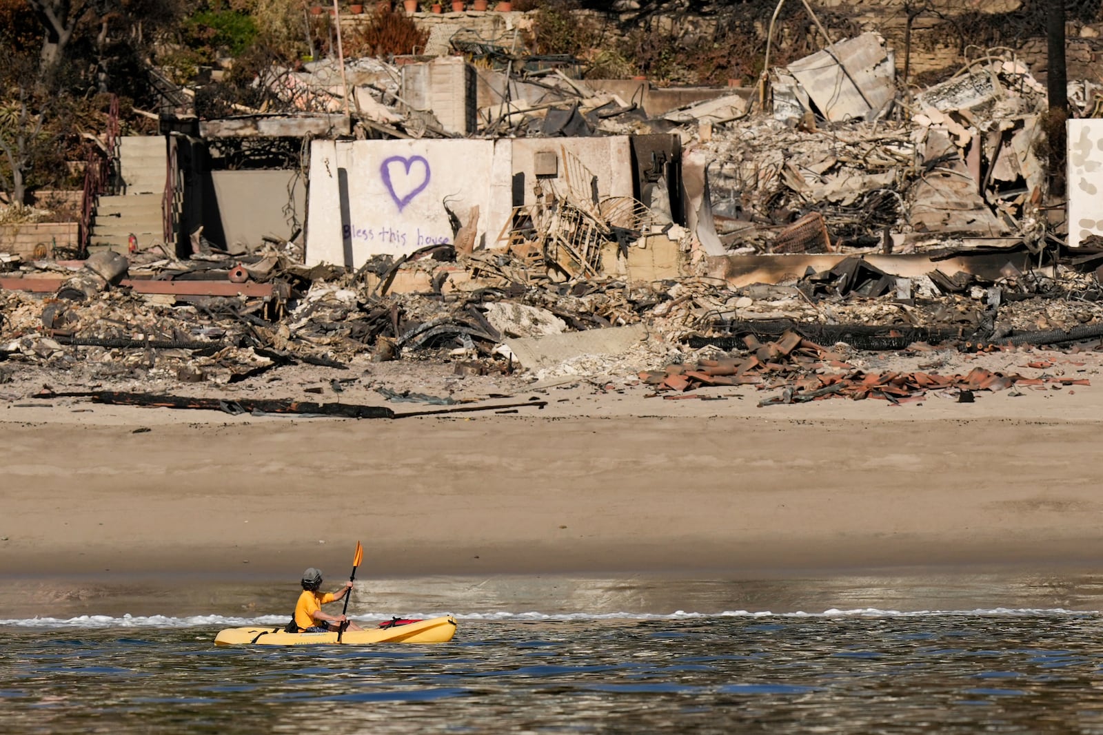 A kayaker goes past a row of homes damaged by the Palisades Fire Wednesday, Jan. 15, 2025 in Malibu, Calif. (AP Photo/Carolyn Kaster)