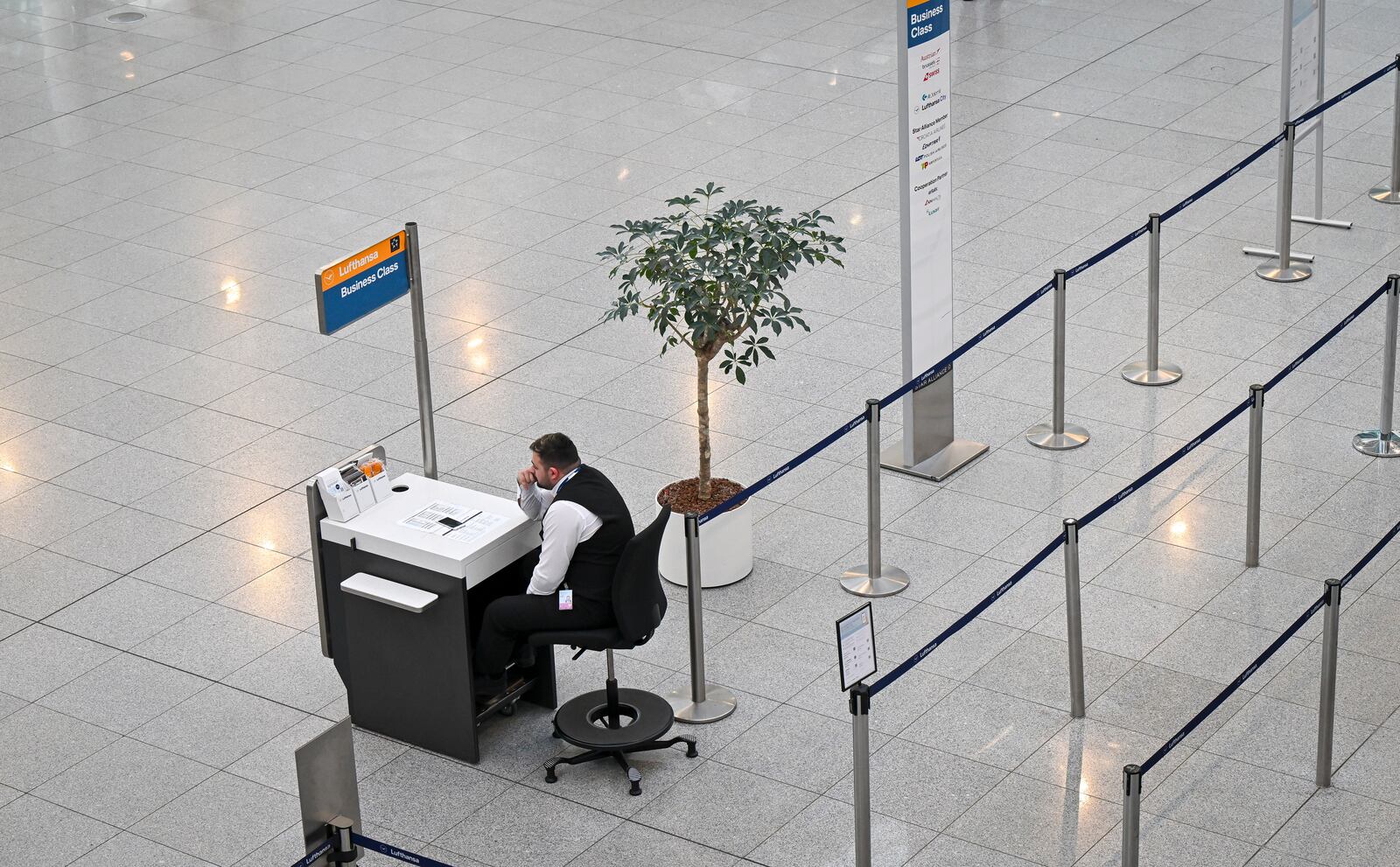 An airport employee sits in front of an empty check-in counter at Terminal 2 at Munich Airport, Germany Monday, March 10, 2025. (Peter Kneffel/dpa via AP)