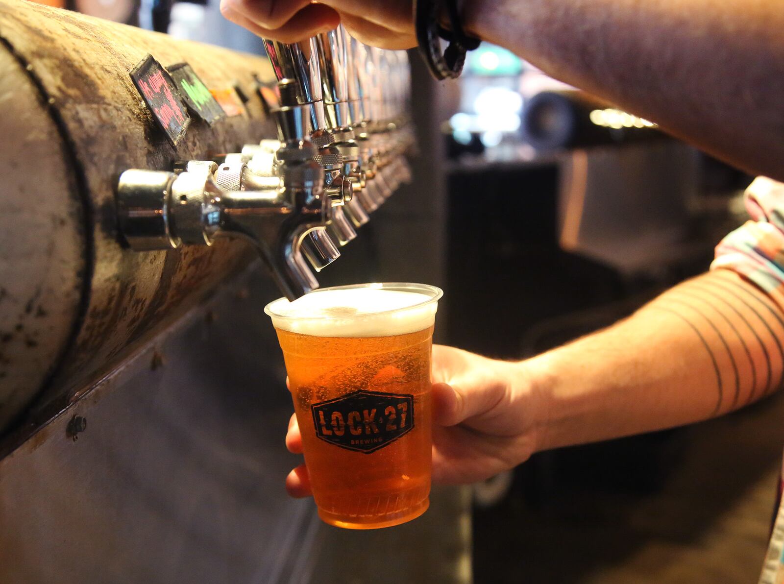 Louis Connelly, a bartender at Lock 27 Brewing in downtown Dayton, pours beer into a plastic cup used in response to the coronaviurs. The restaurant is also using disposable menus, has removed communal salt and pepper shakers and mustard and ketchup bottles from tables and offers plastic cutlery.  LISA POWELL / STAFF