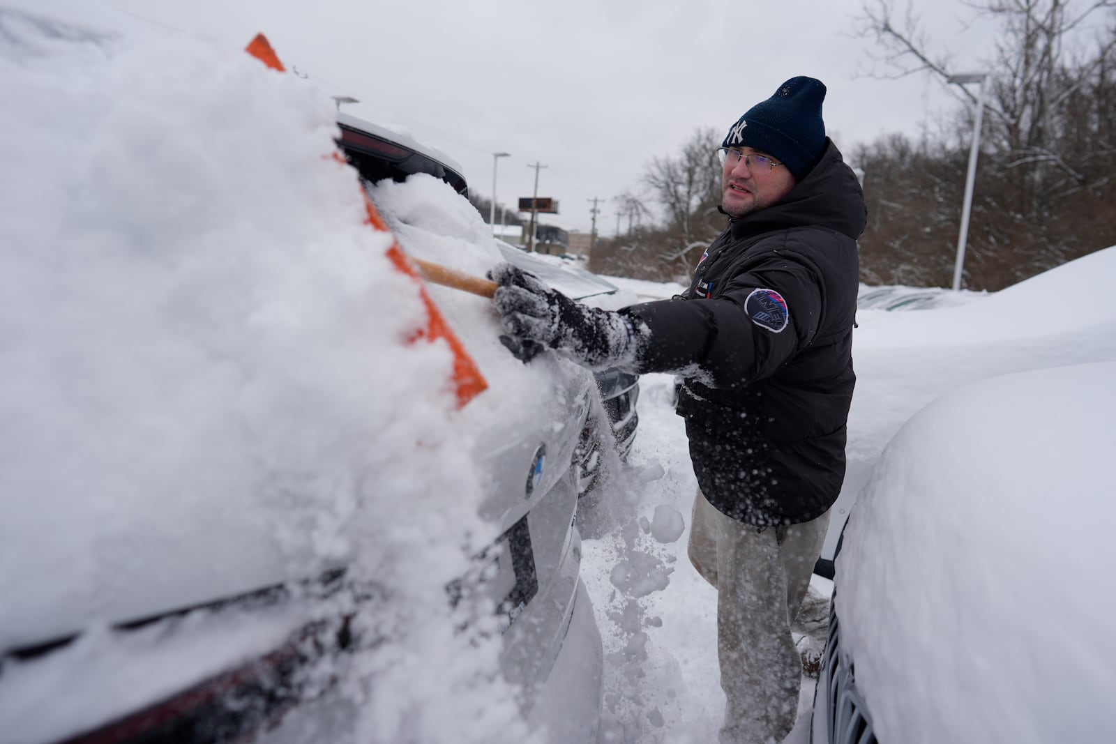 Cary Fallath, the BMW Store lot technician, clears snow from new cars in Silverton, Ohio, Tuesday, Jan. 7, 2025. (AP Photo/Carolyn Kaster)