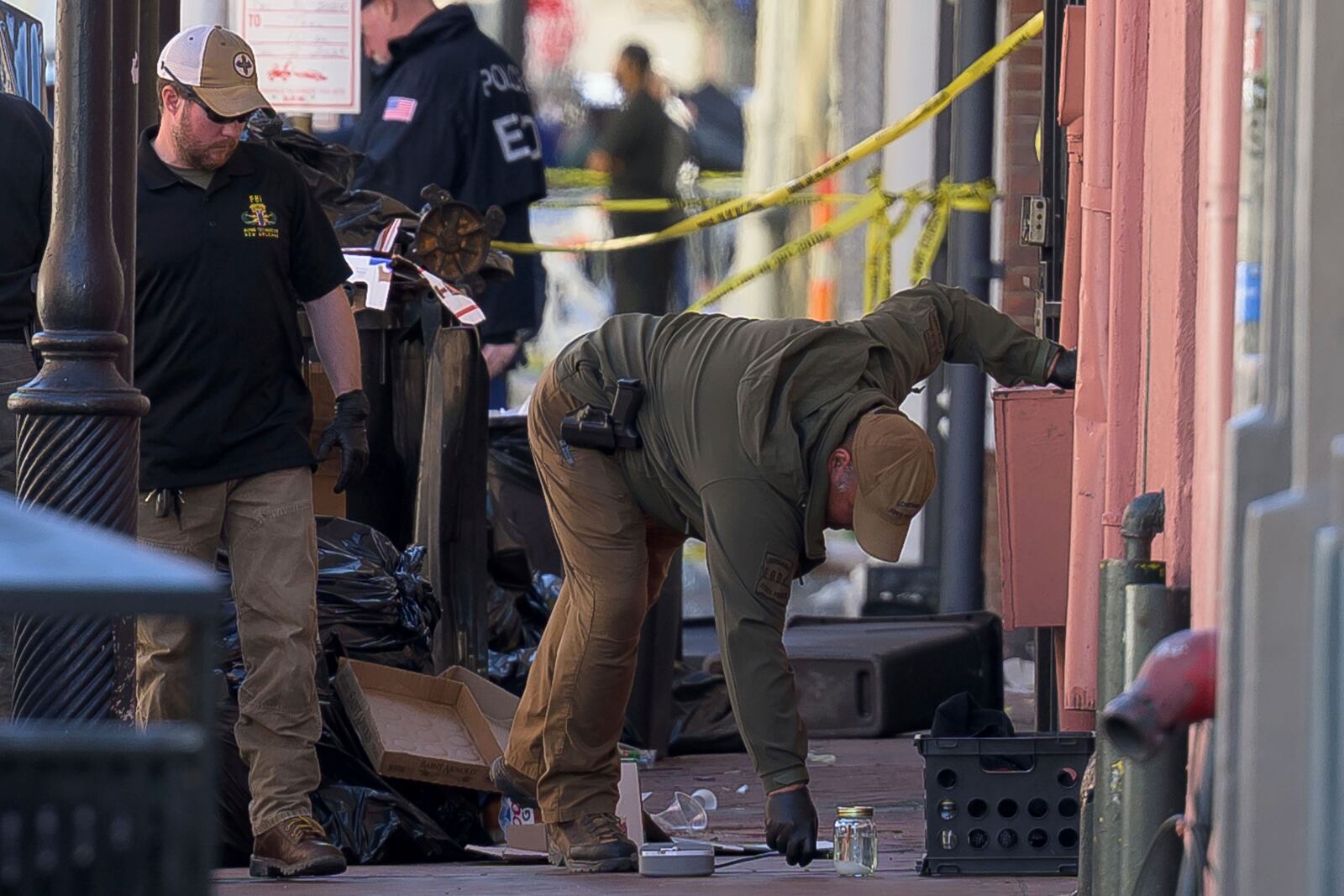 The FBI, left, and Louisiana State Police examine a glass jar along Conti Street that intersects with Bourbon Street during the investigation of a truck crashing into pedestrians on Bourbon Street Wednesday, Jan. 1, 2025. (AP Photo/Matthew Hinton)