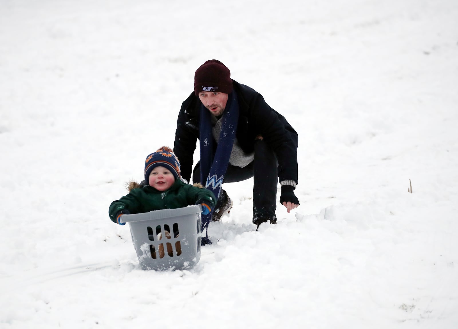 A man is seen with his son as they sledge on a hill with Durham Cathedral which is surrounded by heavy snow in Durham, North East England, as the severe weather continues across England, Sunday, Jan. 5, 2025. (AP Photo/Scott Heppell)