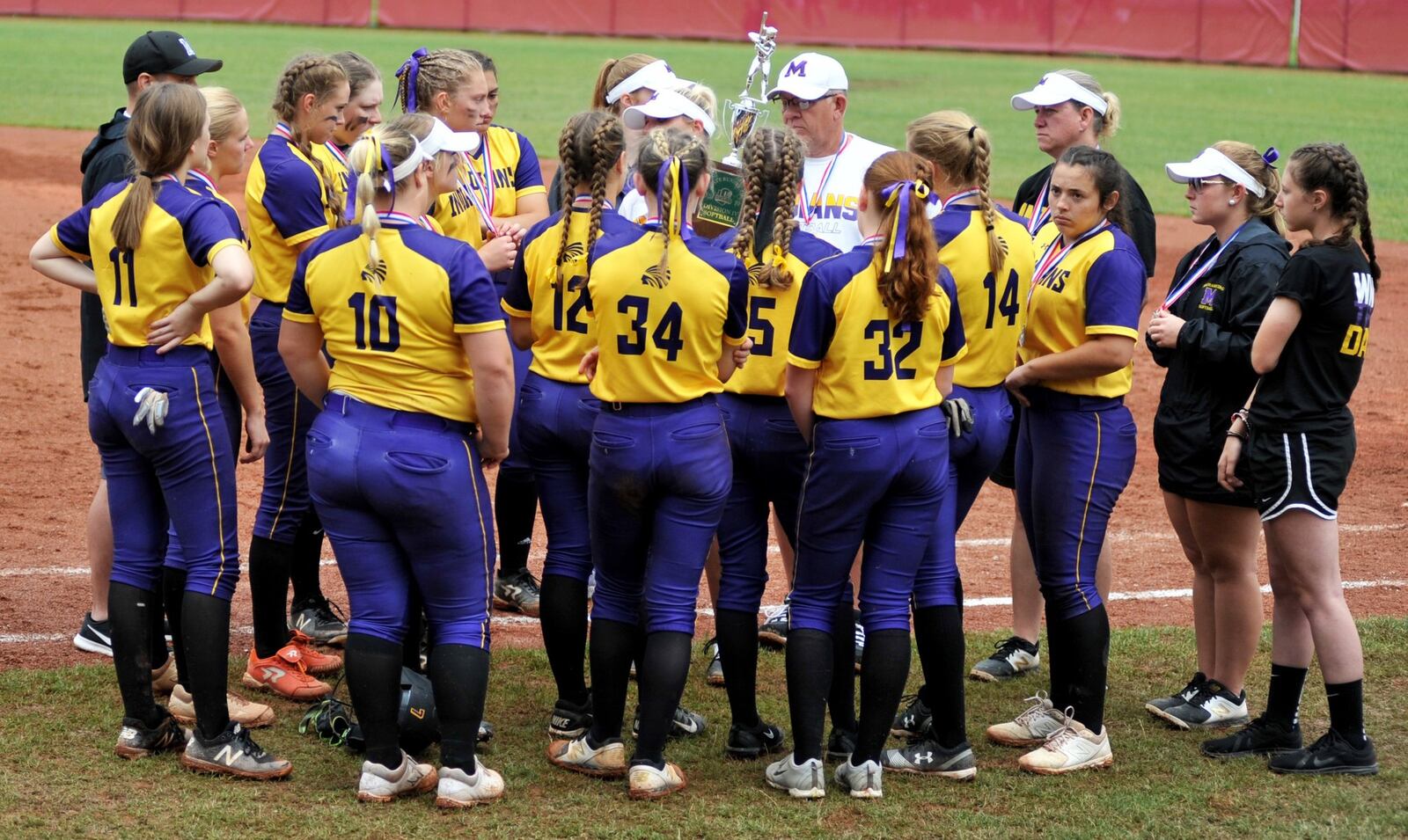 Mechanicsburgh coach Abbey DeLong holds the Division IV state softball runner-up trophy as she talks to her team Sunday after a 5-0 loss to Antwerp at Firestone Stadium in Akron. RICK CASSANO/STAFF