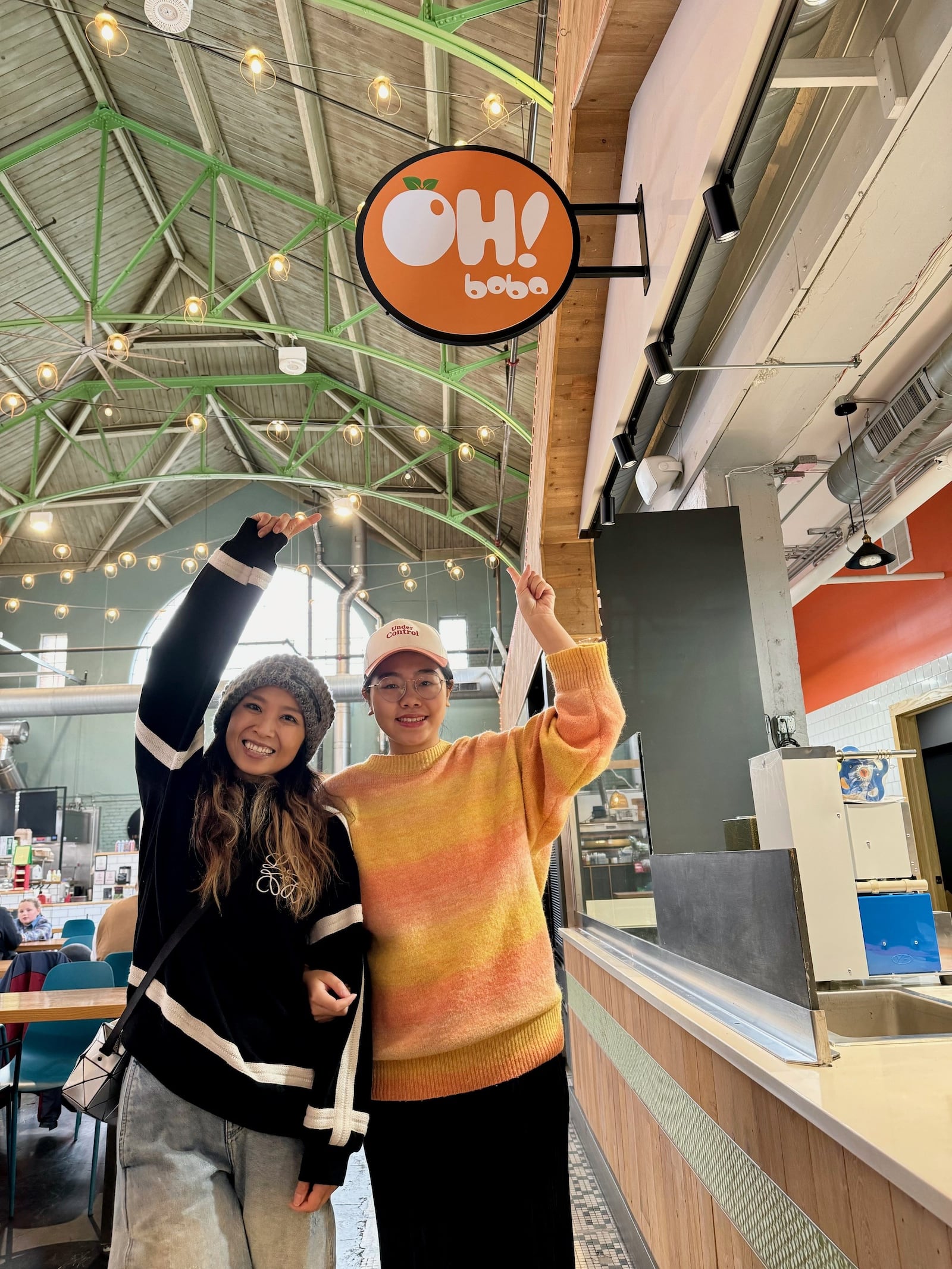 OH! Boba, a tea and smoothie shop, will open in downtown Springfield in COhatch the Market. Two of the three owners, Jess Justice, left, and Ting Shi, point at the new OH! Boba sign that was installed Monday, Nov. 20, 2023. BEN McLAUGHLIN/STAFF