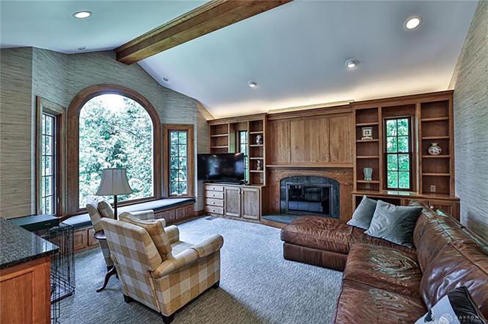 The sunken family room has a vaulted ceiling, woodburning fireplace and carpeting. It also has beams on the ceiling and recessed lighting.