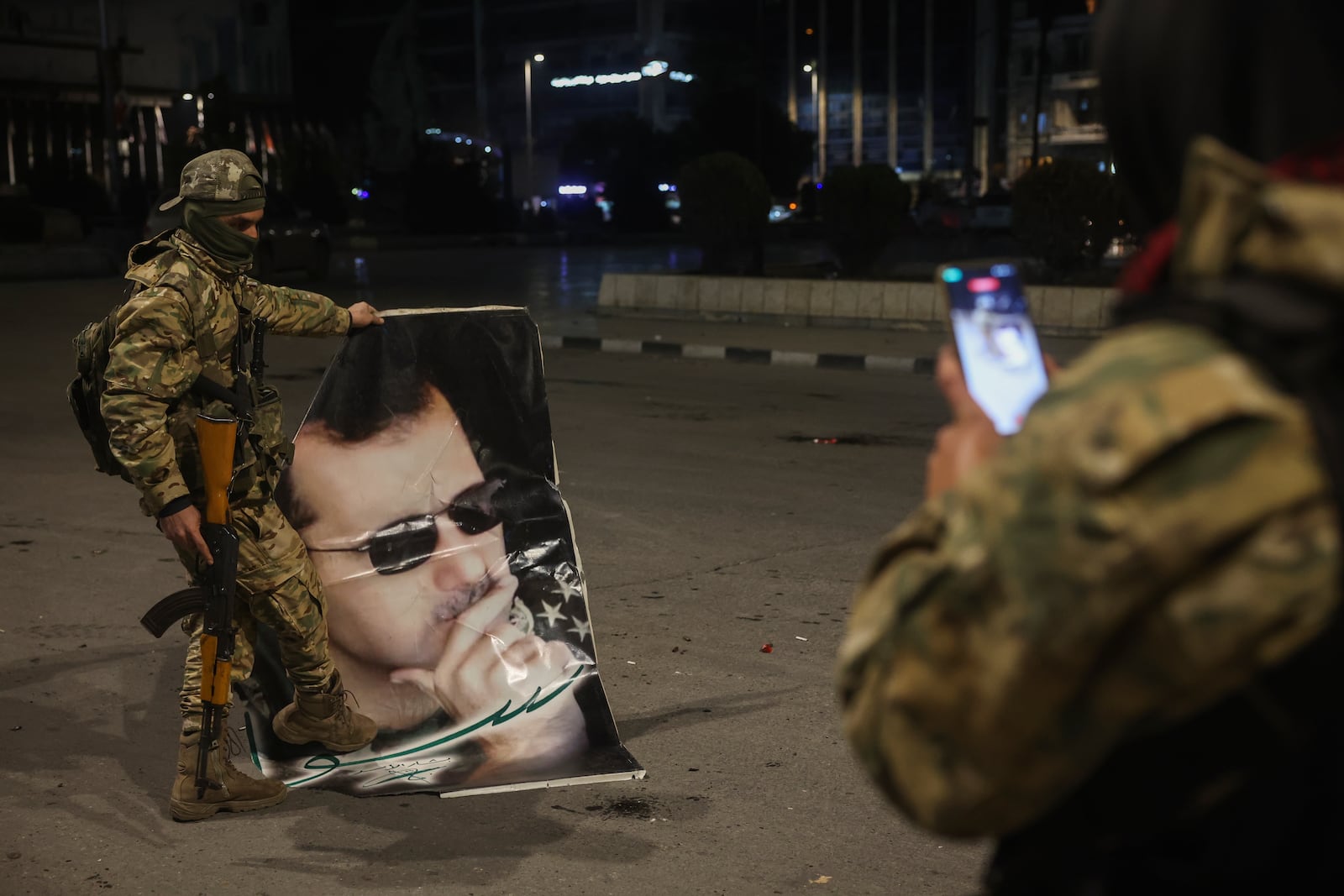 A Syrian opposition fighter takes a picture of a comrade stepping on a portrait of Syrian President Bashar Assad in Aleppo, early Saturday Nov. 30, 2024. (AP Photo/Ghaith Alsayed)