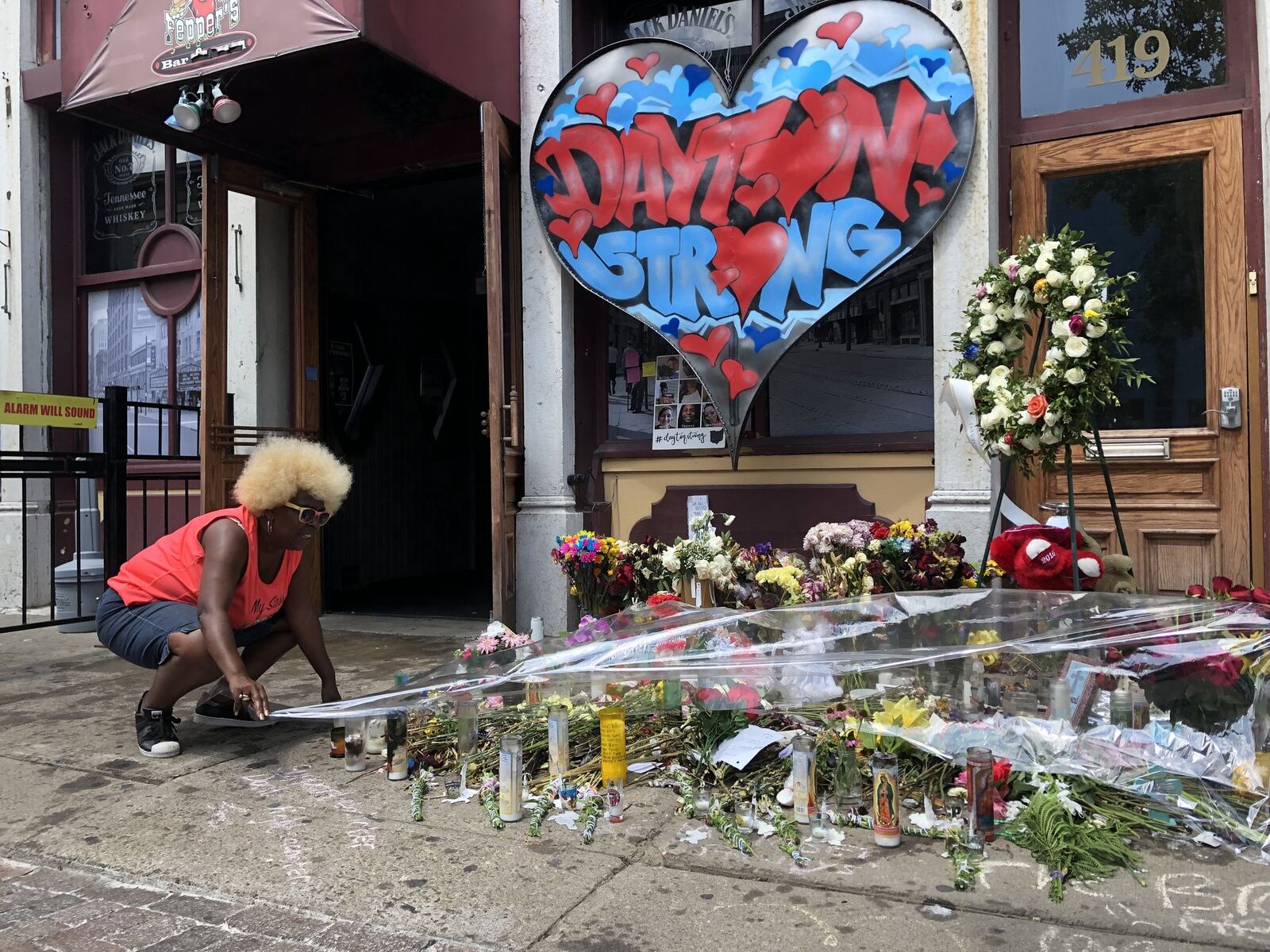 Annette Gibson-Strong covers a memorial for the Oregon District mass shooting victims on Thursday afternoon as the threat of rain approached. BONNIE MEIBERS / STAFF