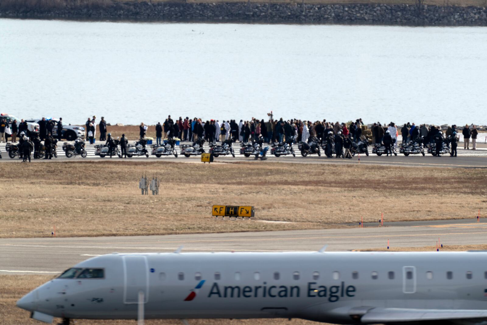 An American Eagle jet passes as families of the victims of a mid-air collision between an American Airlines jet and an Army helicopter stand near the wreckage site in the Potomac River at the end of the runway 33 from Ronald Reagan Washington National Airport, Sunday, Feb. 2, 2025, in Arlington, Va. (AP Photo/Jose Luis Magana)