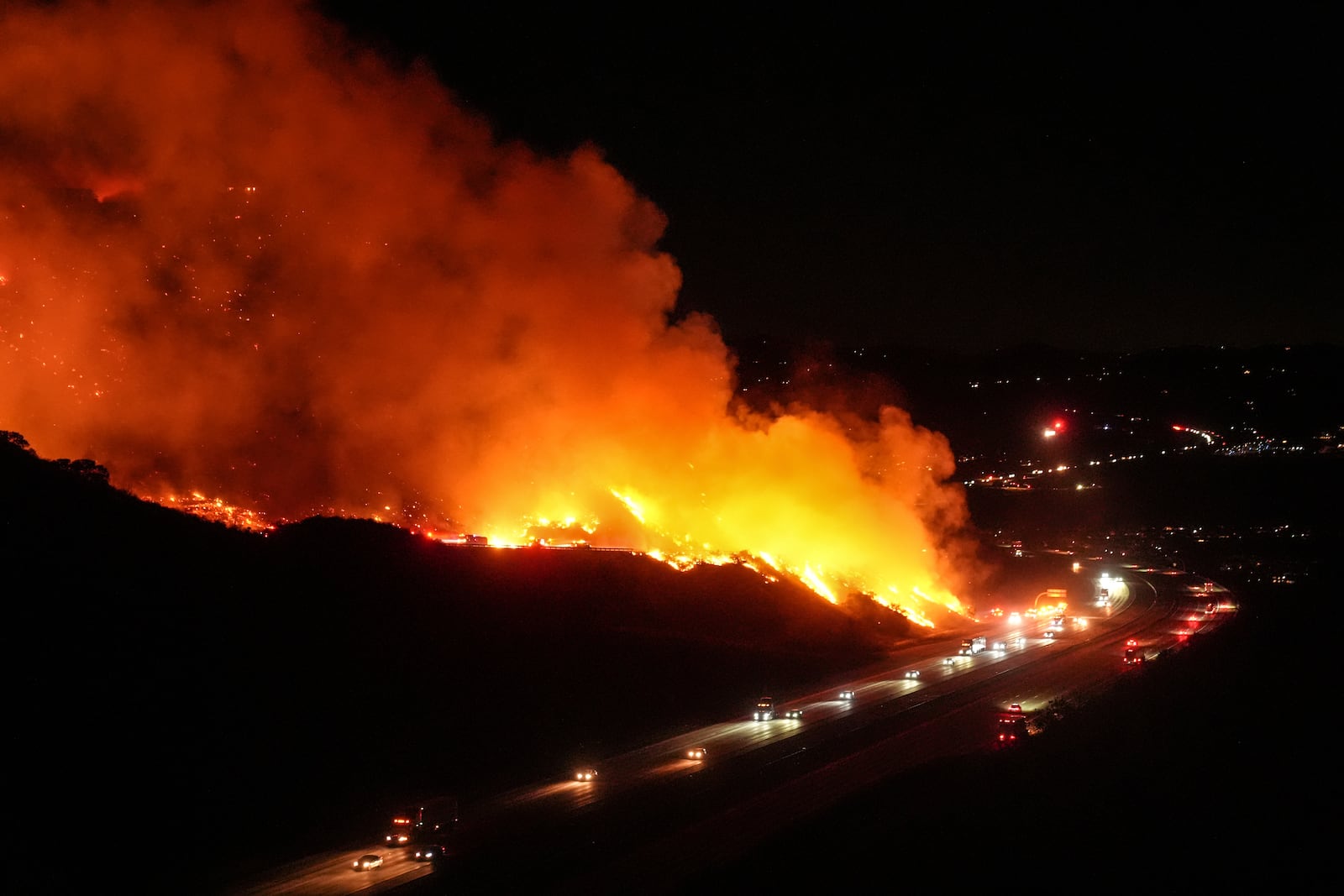 Vehicles drive along Interstate 15 as the Lilac Fire burns along a hillside in Bonsall, Calif., Tuesday, Jan. 21, 2025. (AP Photo/Jae C. Hong)