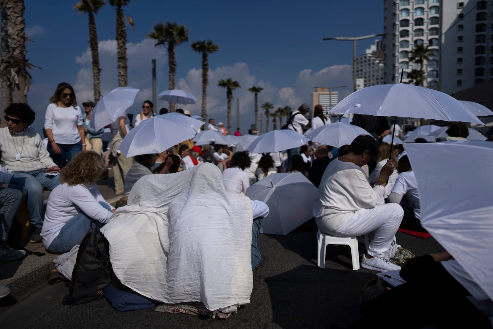 Activists sit on a road with white umbrellas during a protest calling for the release of hostages held in the Gaza Strip, in front of the U.S. Embassy branch office in Tel Aviv, Israel, Friday, Jan. 31, 2025. (AP Photo/Oded Balilty)