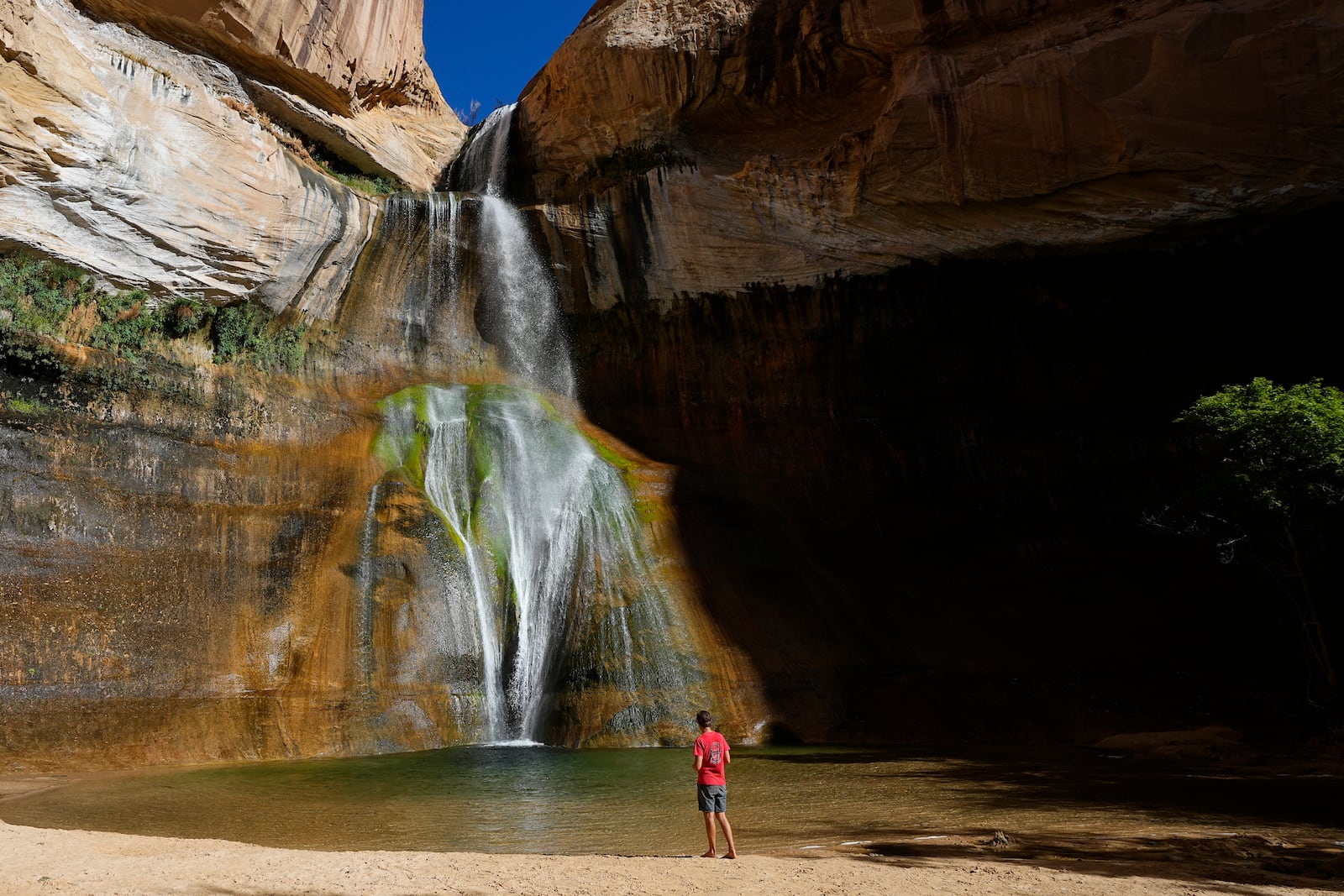 FILE - A hiker watches a waterfall at Lower Calf Creek Falls at Grand Staircase Escalante National Monument Wednesday, July 12, 2023, in Escalante, Utah. (AP Photo/Ross D. Franklin, File)