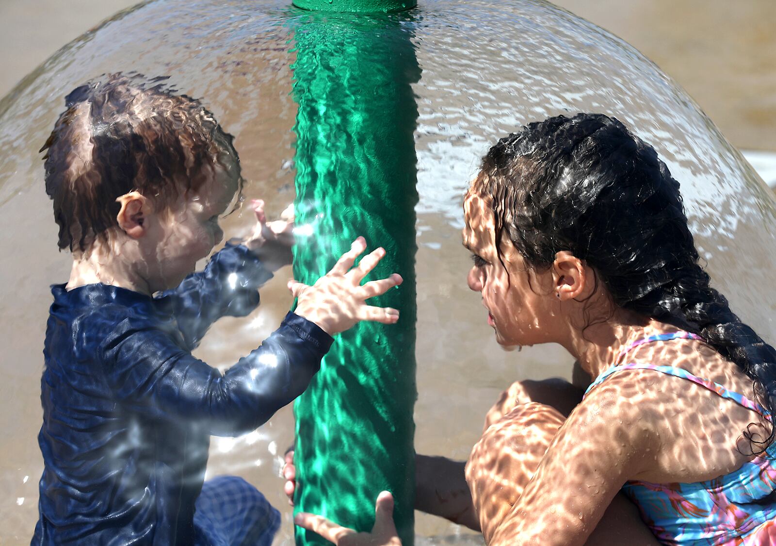 Piper Lane sits with her brother, Briggs, under one of the water features on the Snyder Park Sprayground Wednesday, June 15, 2022. The Sprayground opened for the first time this season on Wednesday. It had been out of commission since last year but National Trail Parks and Recreation got it repaired just in time for one of the hottest days of the year. BILL LACKEY/STAFF