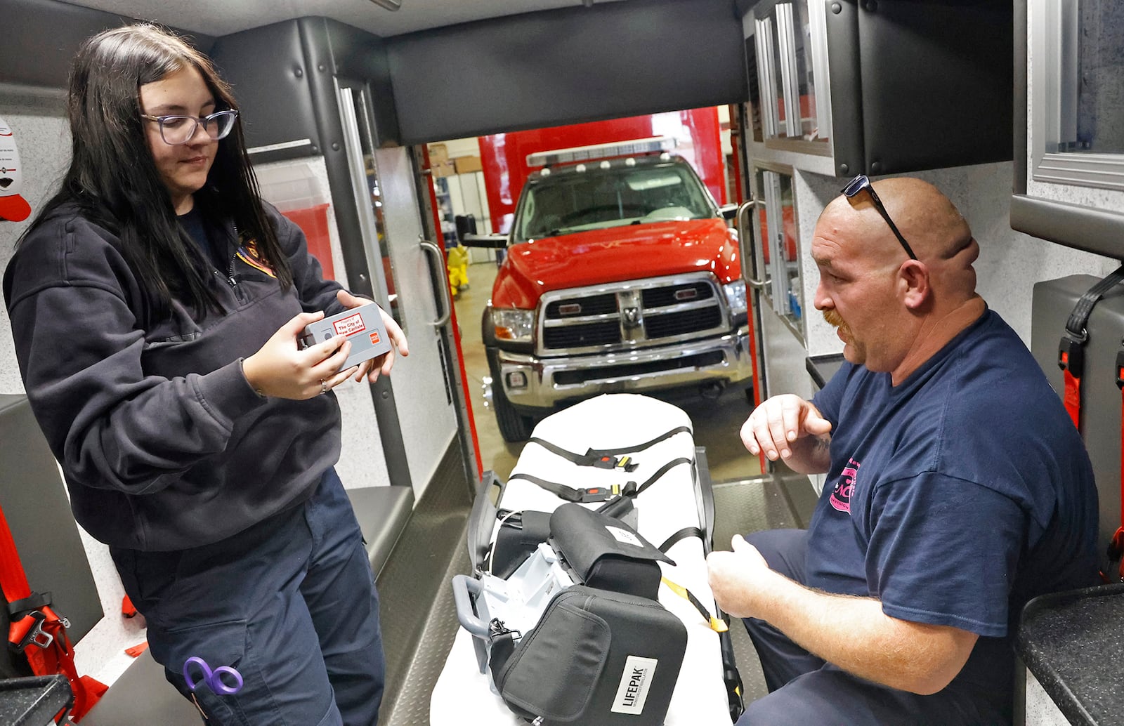 Riayn Lowrey, the New Carlisle Fire Department's newest recruit, looks over the rechargeable battery for a heart monitor as Firefighter/ EMT Kevin Stephens shows her the equipment in a medic unit Thursday, Sept. 7, 2023. BILL LACKEY/STAFF