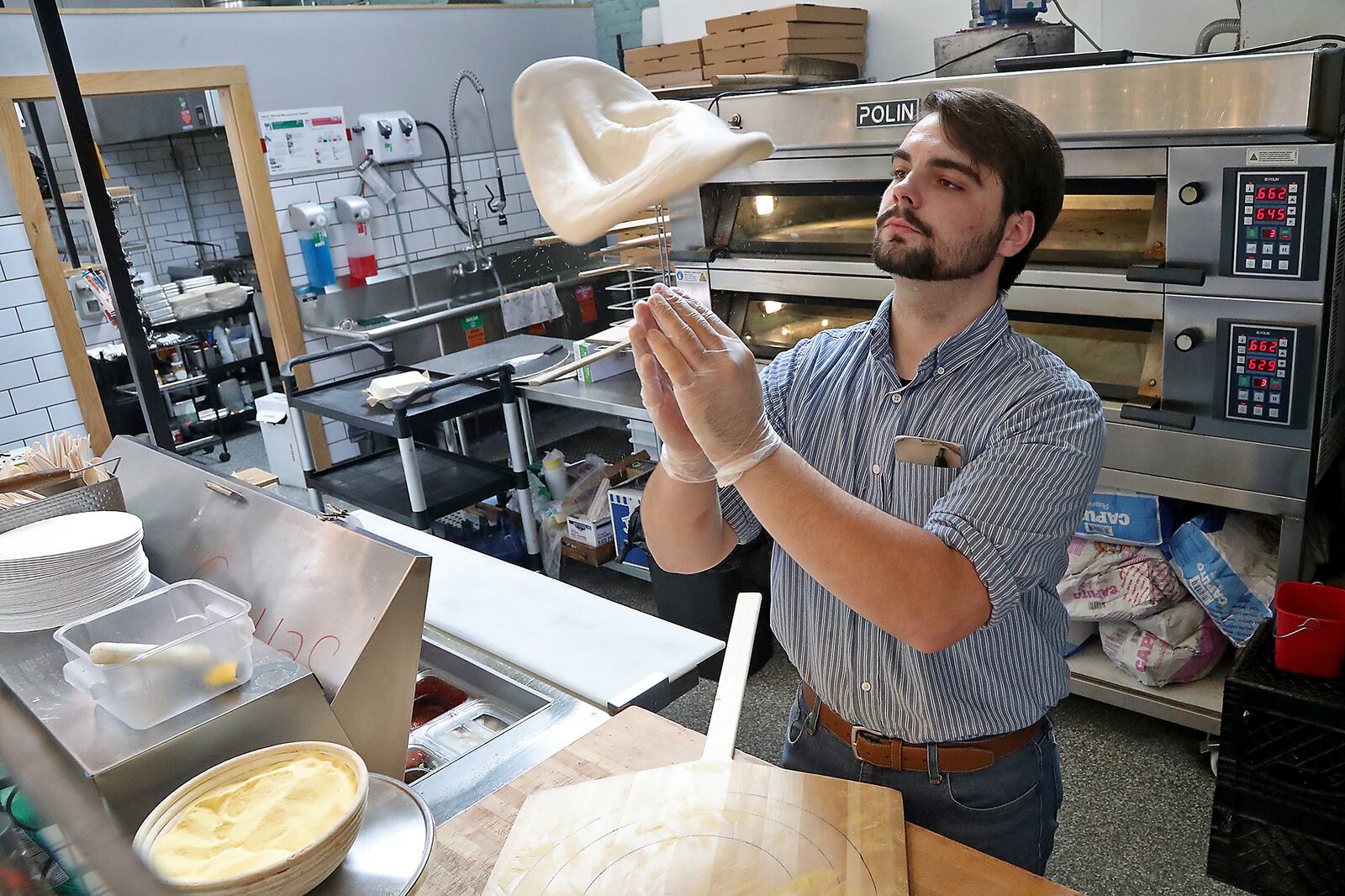 Ryan Thomas, an employee of Crust & Company in the Springfield COhatch, makes a pizza for a customer  June 16, 2022. BILL LACKEY/STAFF