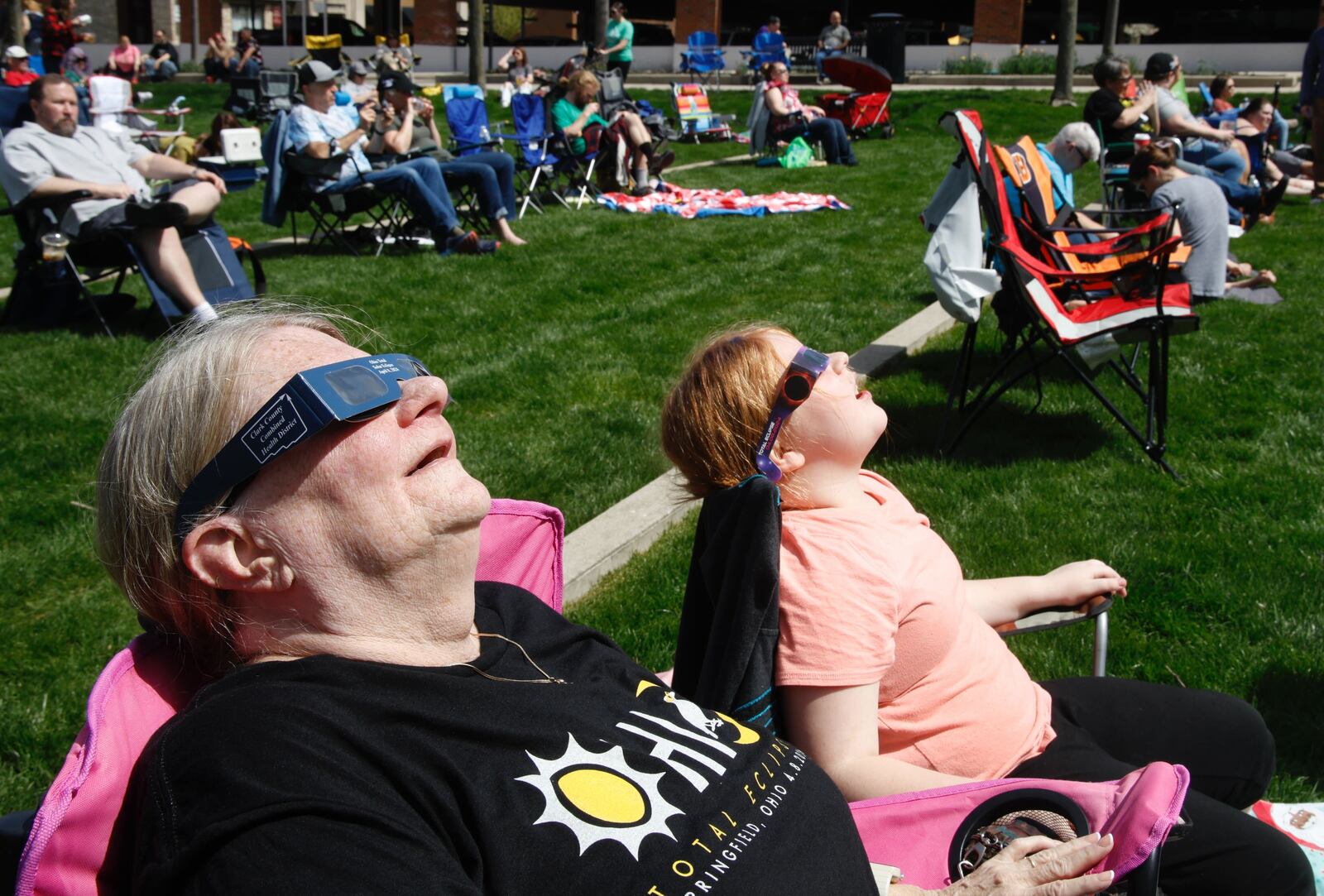 Brenda Holbrook and her granddaughter, Ella, keep an eye on the sun while wearing their eclipse glasses Monday, April 8, 2024, at the eclipse watch party at National Road Commons Park in downtown Springfield. BILL LACKEY/STAFF